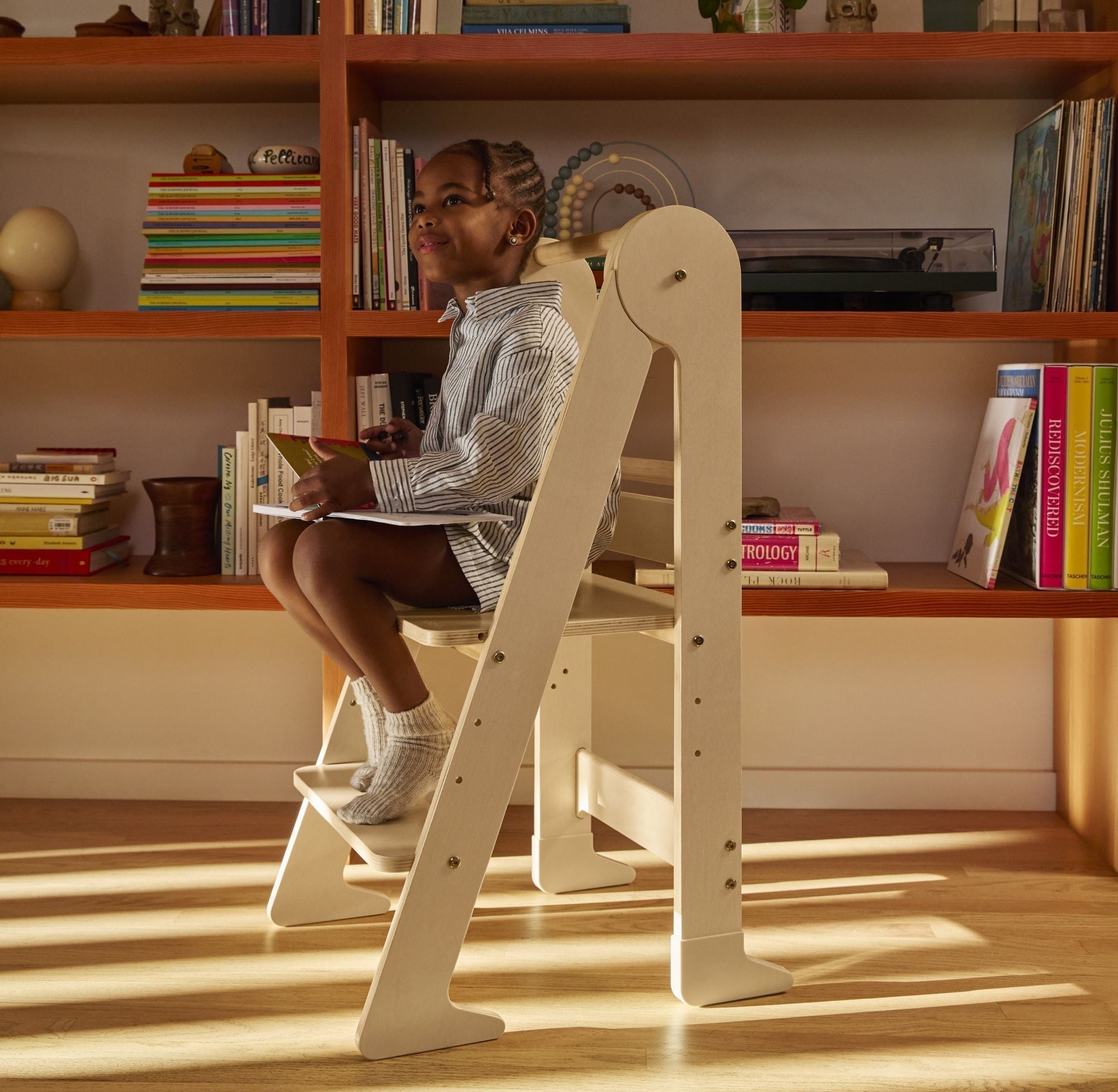 Child enjoying a screen free activity reading a book while sitting on a Piccalio toddler tower made of natural wood