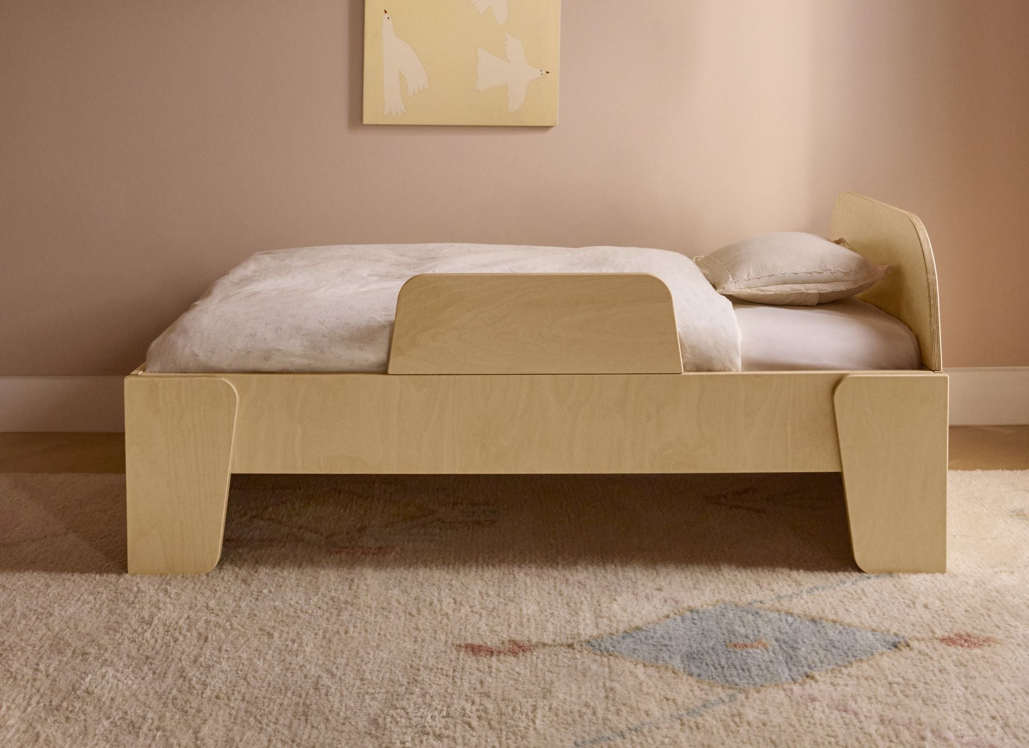 Piccalio toddler bed with a safety rail in a Montessori bedroom with neutral carpet and walls.