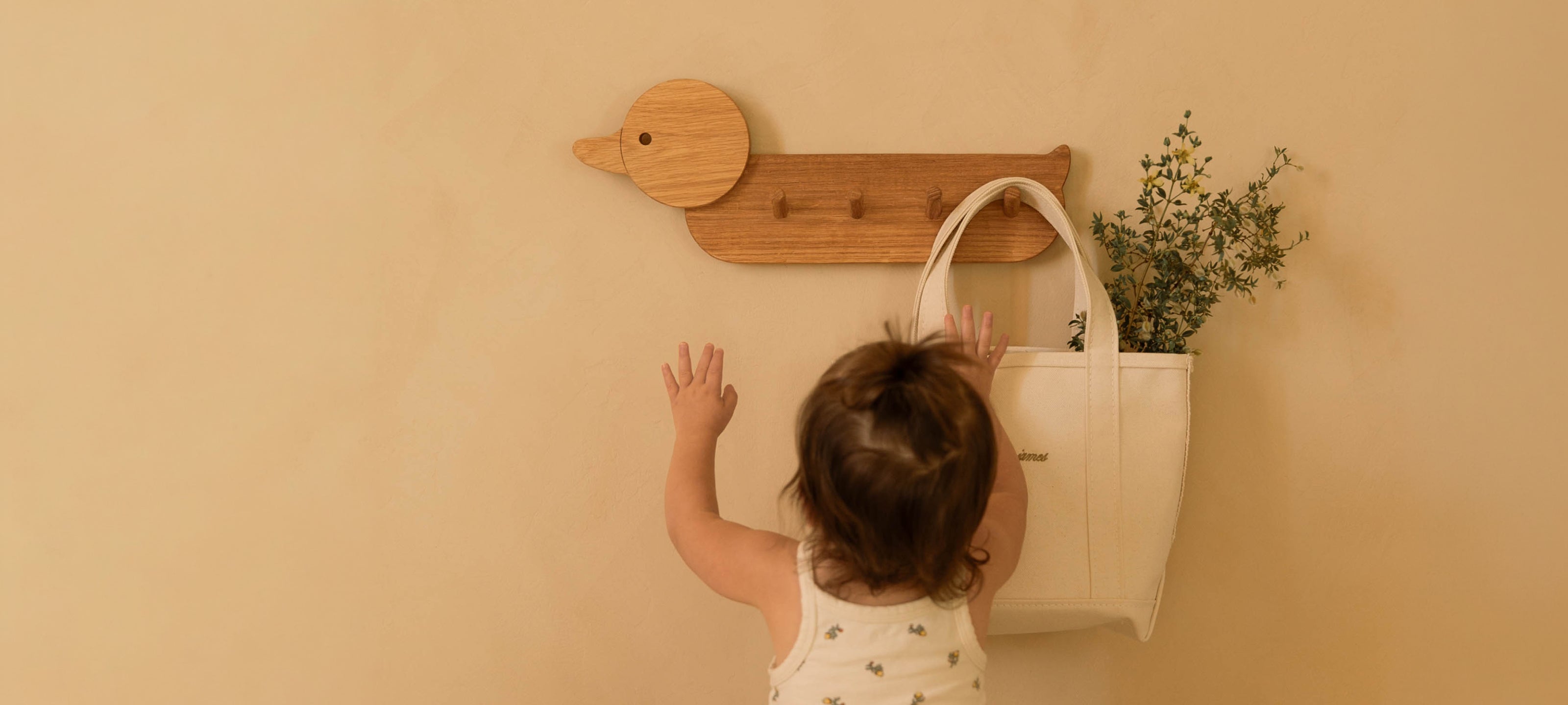 Toddler hangs a tote bag on the duck shaped Piccalio coat rack featuring four coat hooks for children