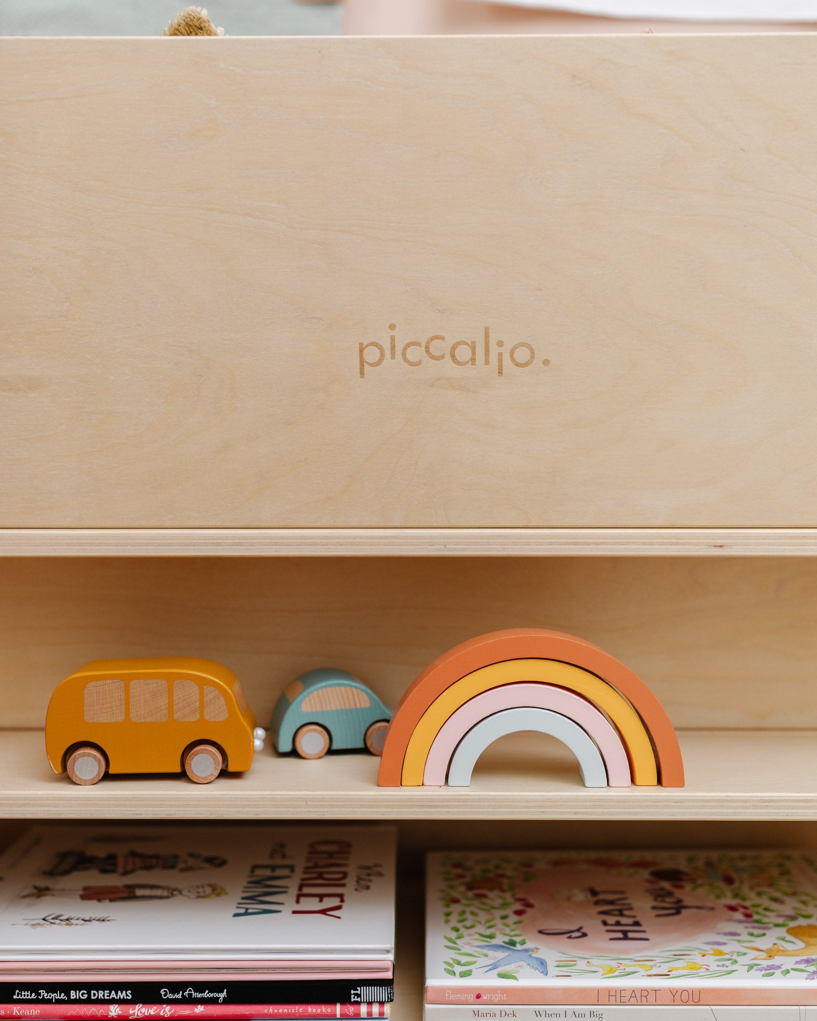 Close-up of the Piccalio wooden Montessori bookshelf showing the rear storage shelves with wooden rainbow blocks and cars.