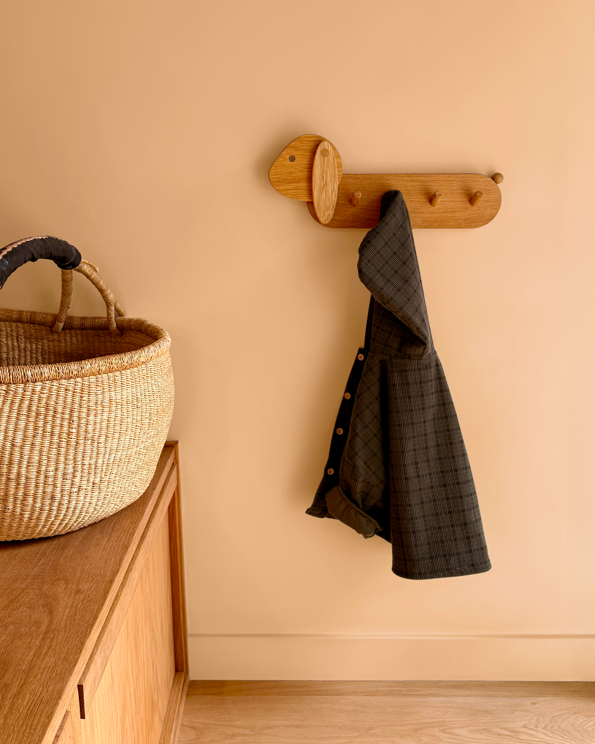 A coat hangs on the bunny shaped Piccalio coat rack for children made of natural oak wood and a non-toxic finish.