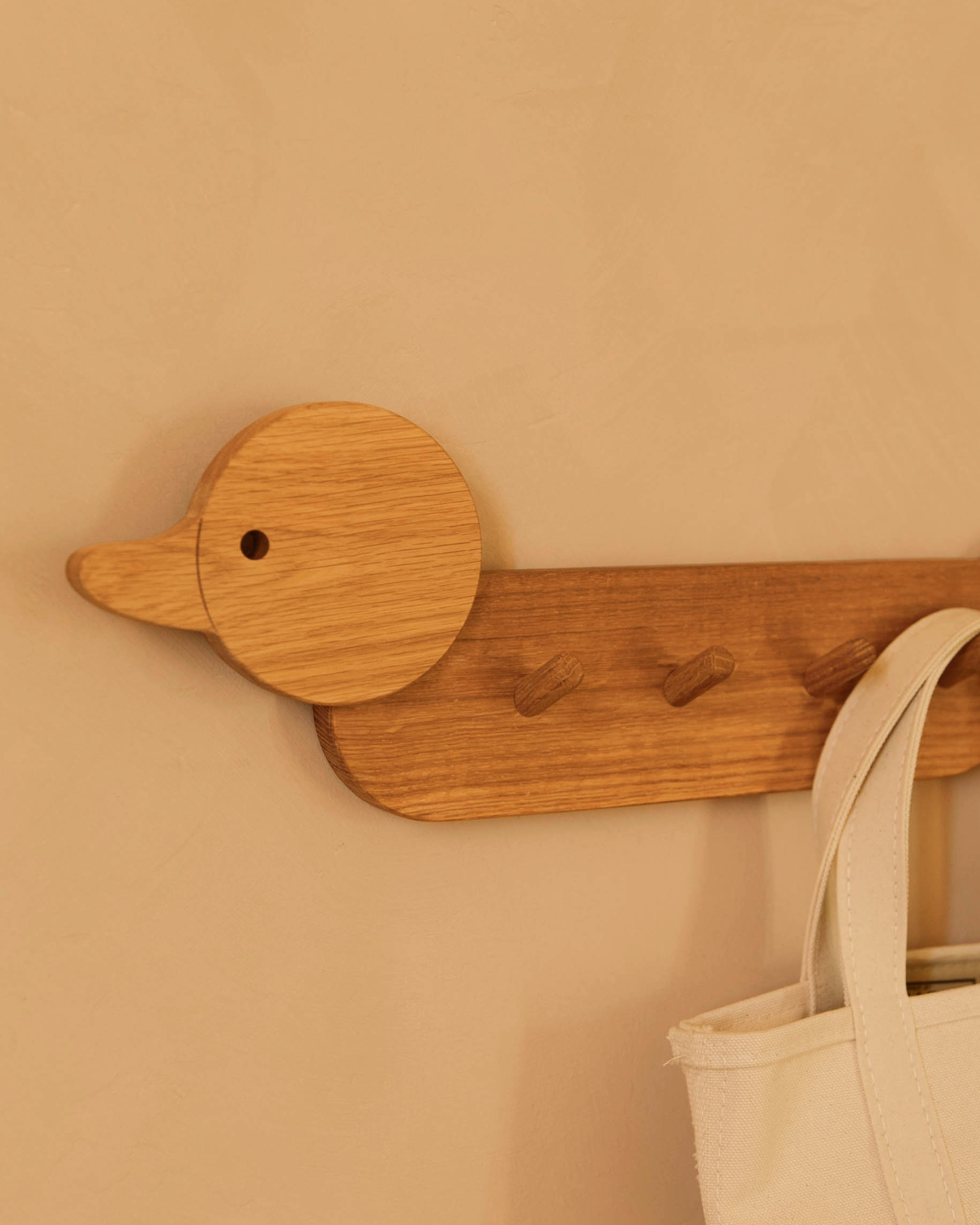 Piccalio duck shaped children's coat rack with a canvas bag hanging on one of the four hooks