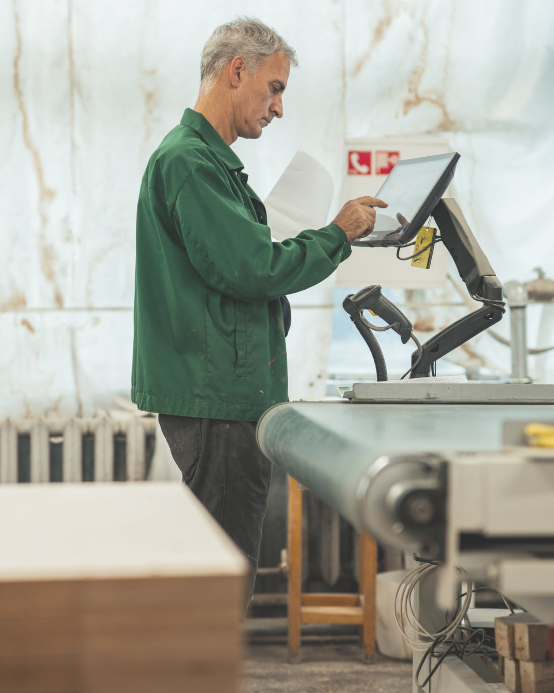 Man in a green jacket using a computer in an industrial setting