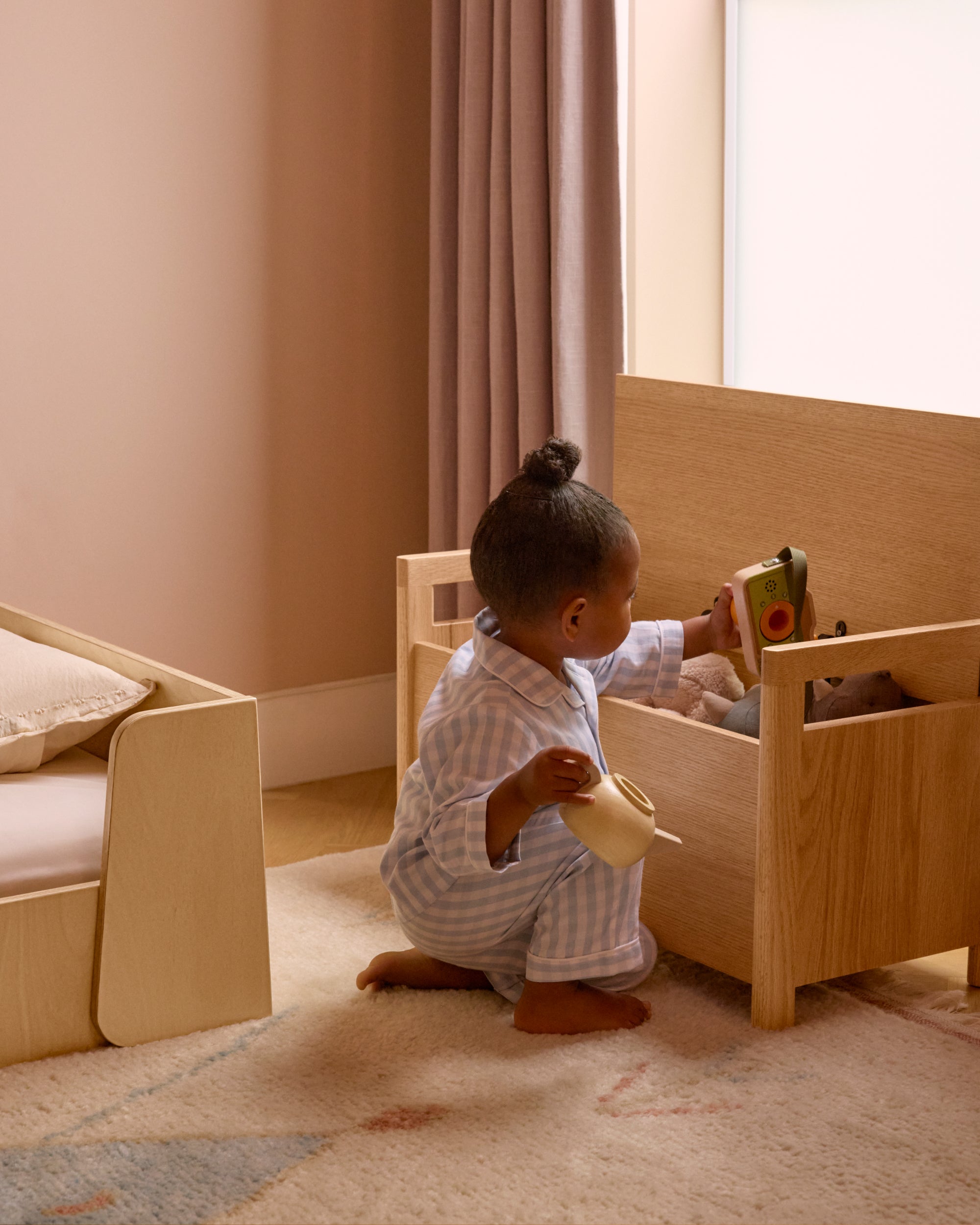 Toddler reaching for toys inside a Piccalio oak toy box, promoting independent play.