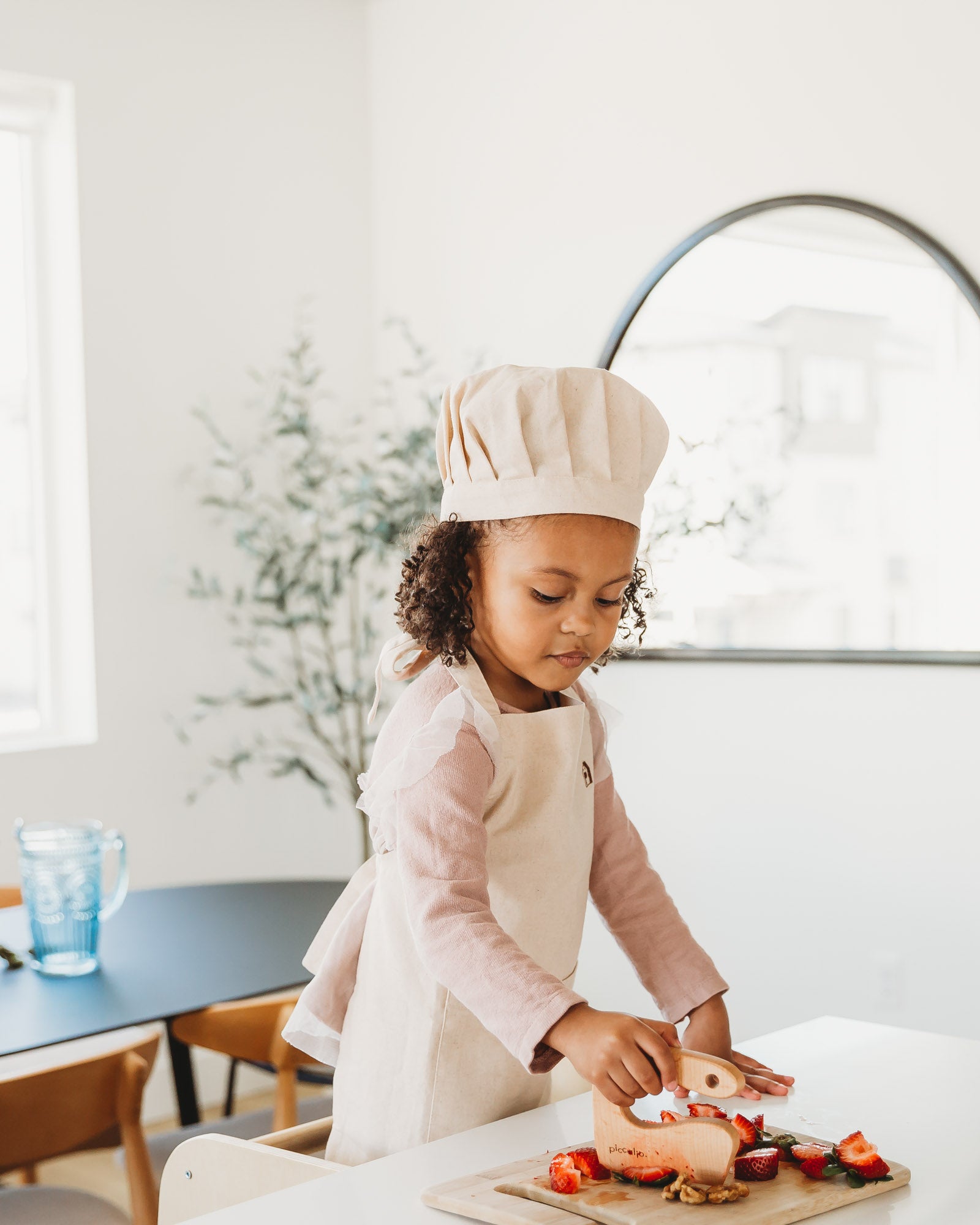 Piccalio apron and hat set from organic linen word by a girl in the kitchen cutting fruit using a Piccalio mini cutter knife.