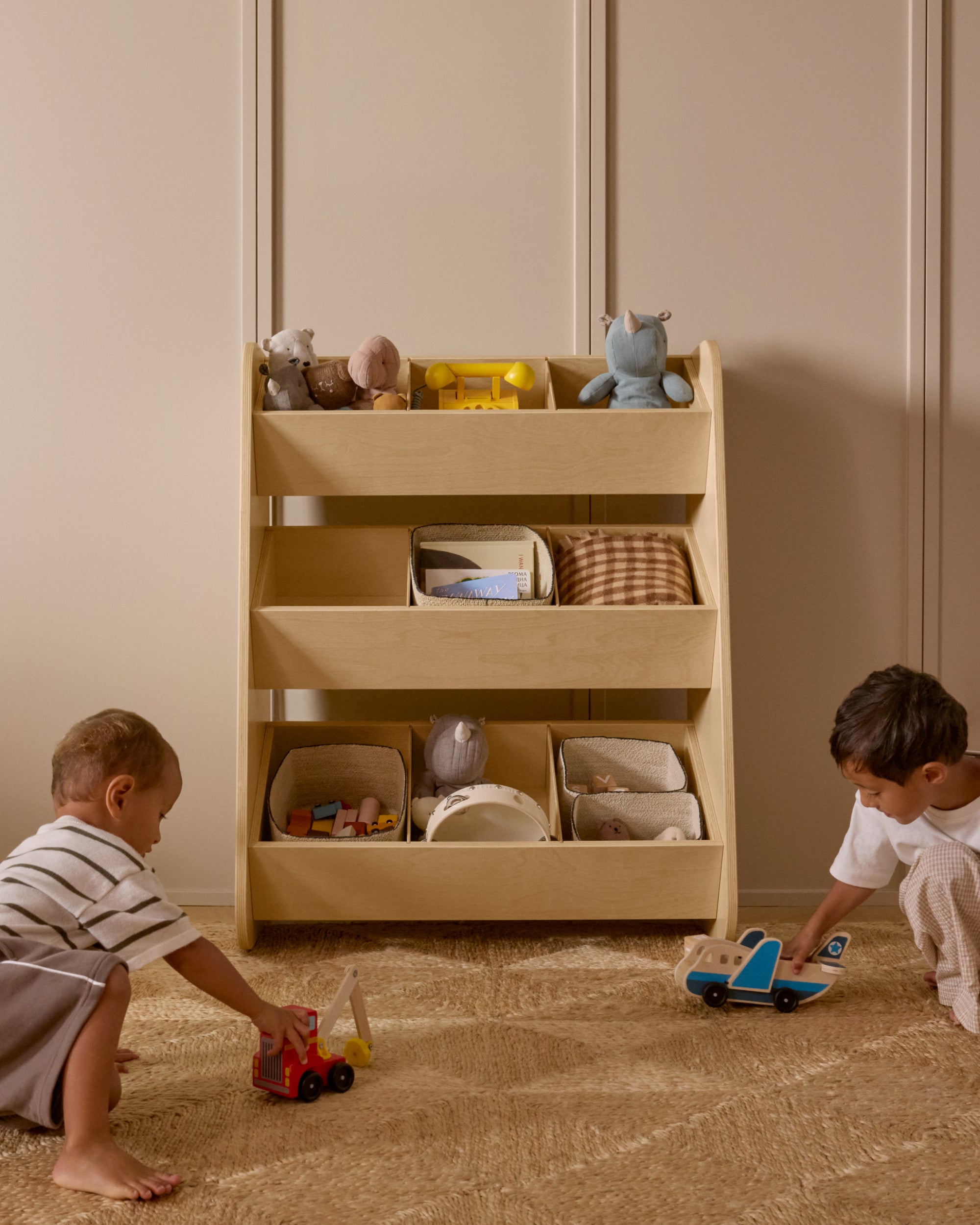 Two children playing with toys in front of a Piccalio birchwood tiered toy organizer in a kid's room.