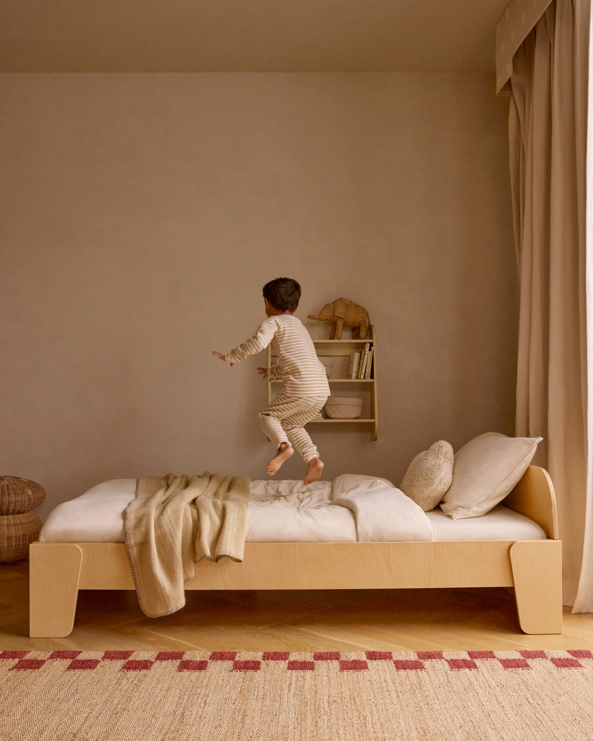 Piccalio Montessori floor bed in natural wood with a child jumping on the bed.