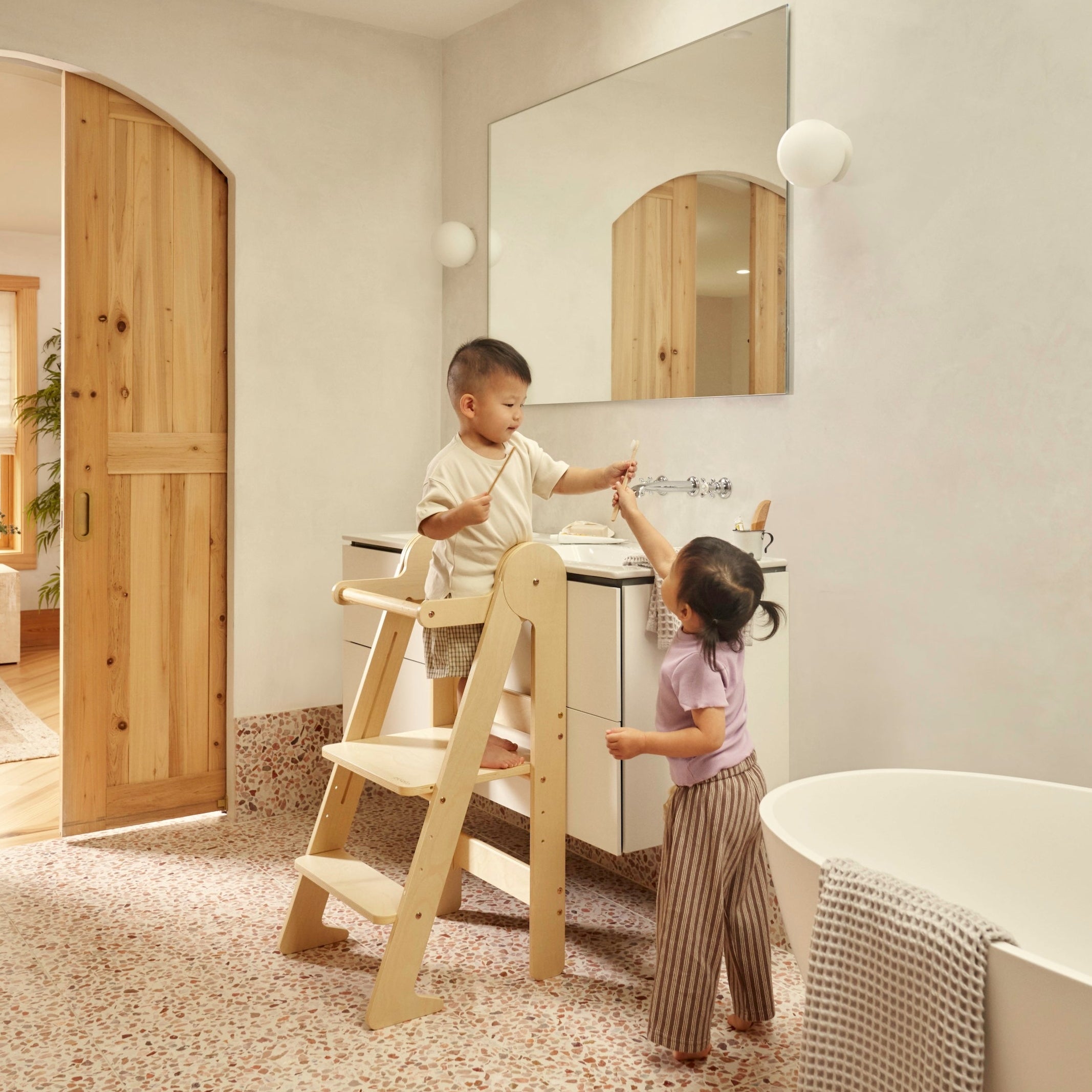 Toddler using a wooden learning tower at a bathroom sink for independent hand washing.