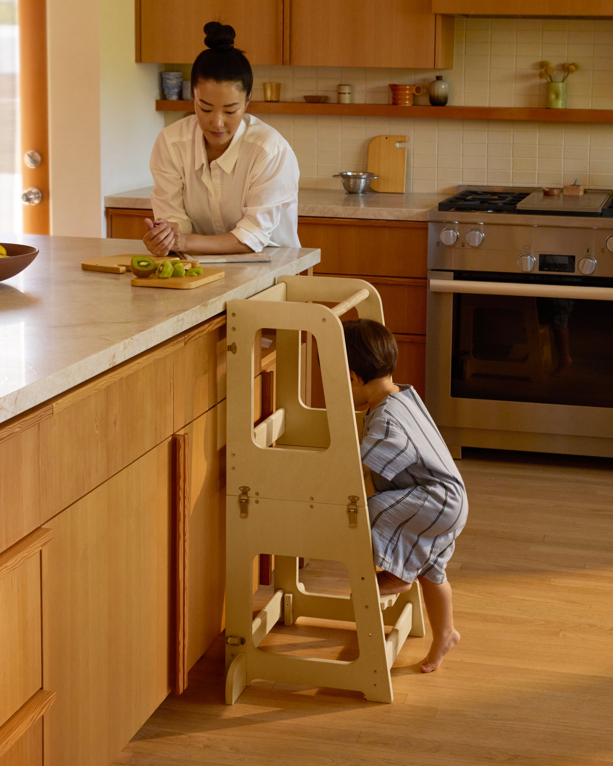 Piccalio convertible toddler tower with a toddler climbing on the tower with the mother by his side.