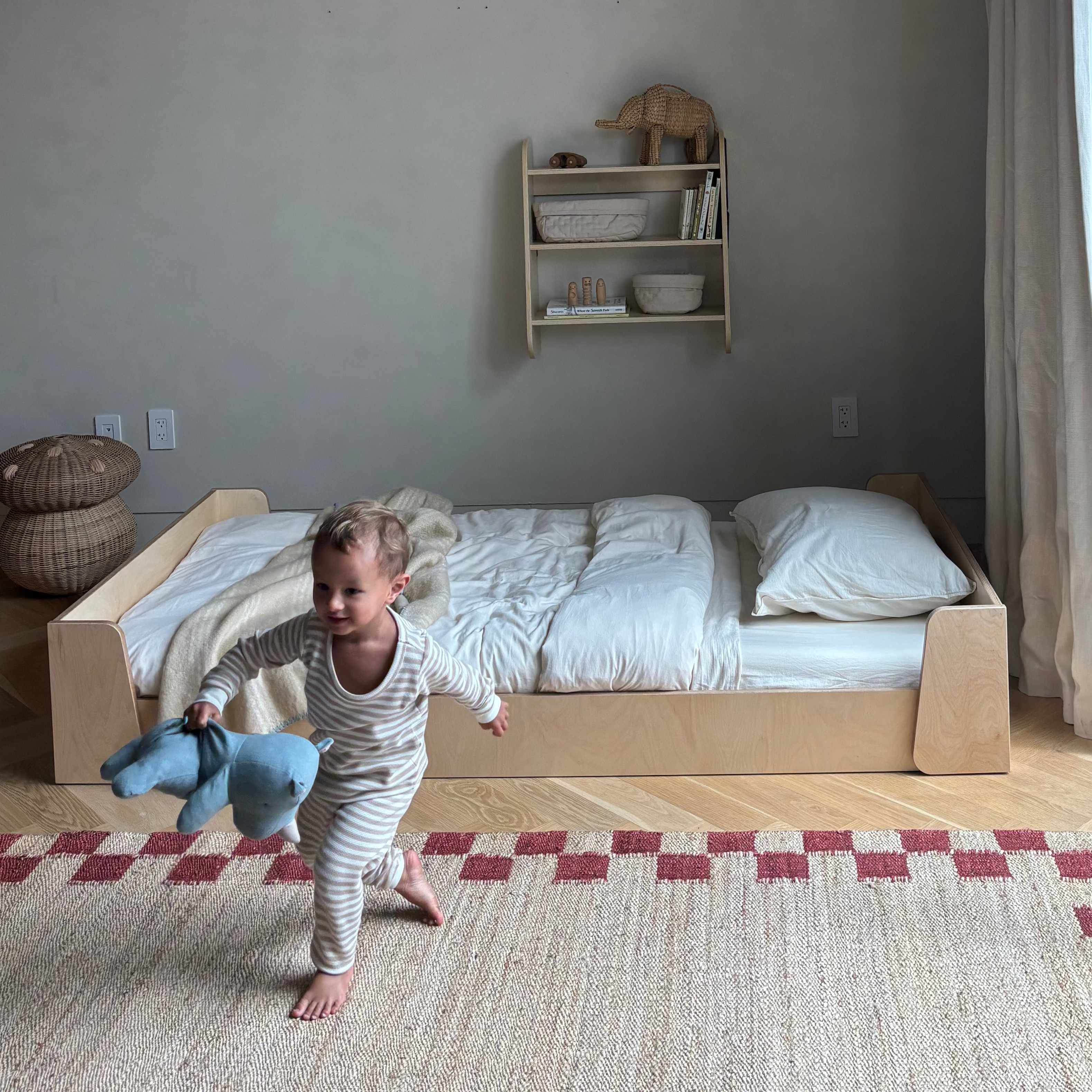 Toddler playing in a bedroom with a montessori floor bed and shelves.