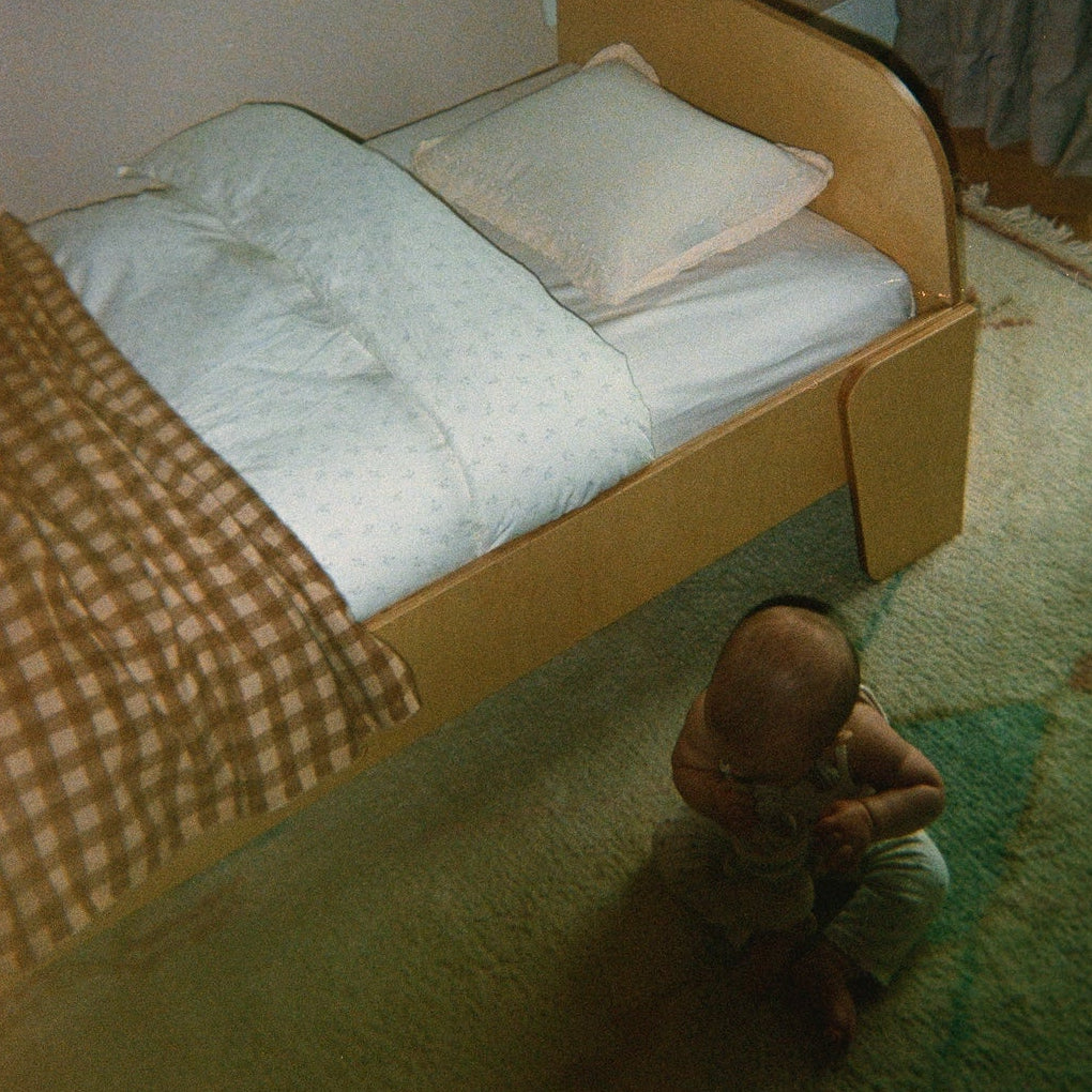 Child playing on a green carpeted floor next to a piccalio montessori floor bed