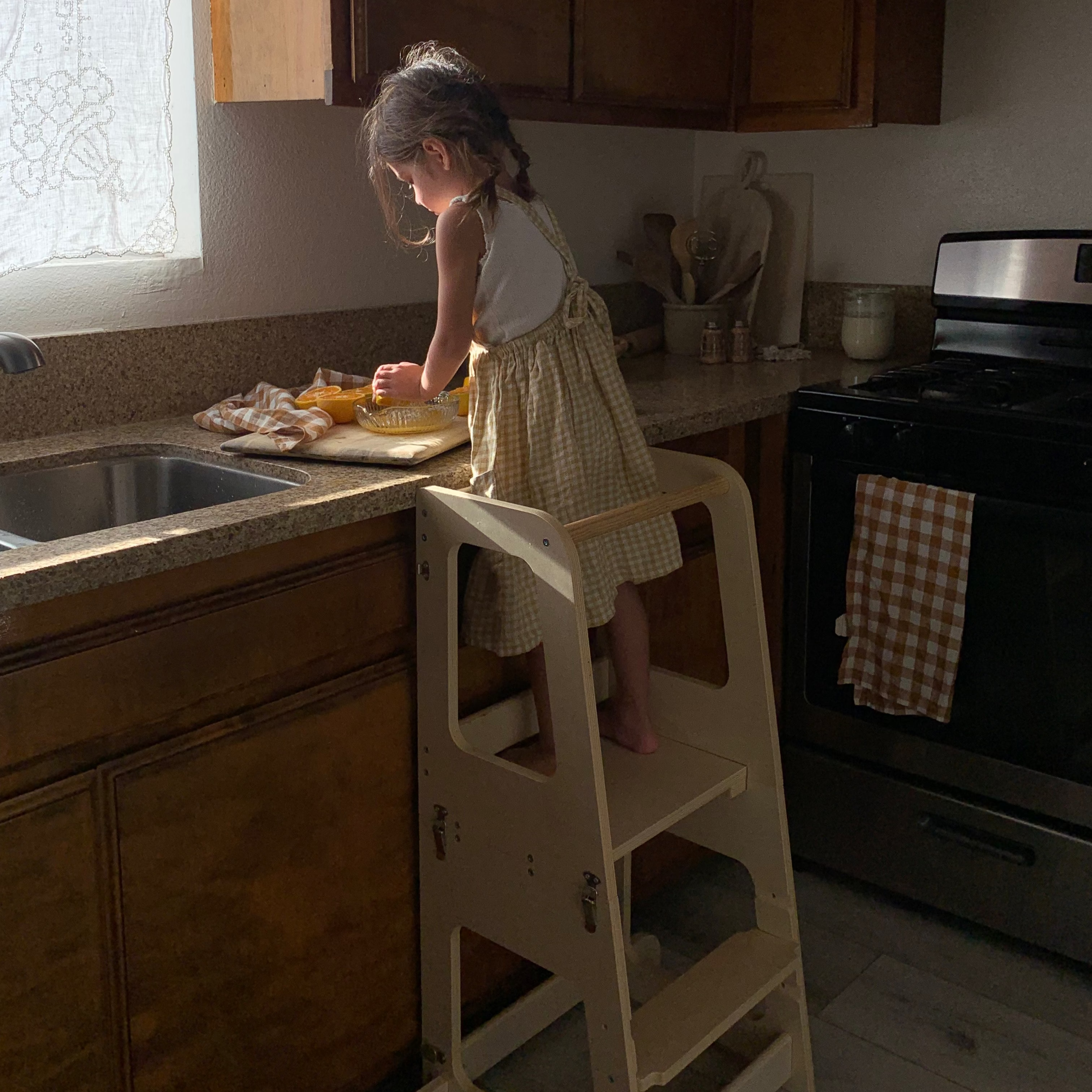 Piccalio Convertible Toddler Tower in natural wood with a Toddler standing on the tower making food.