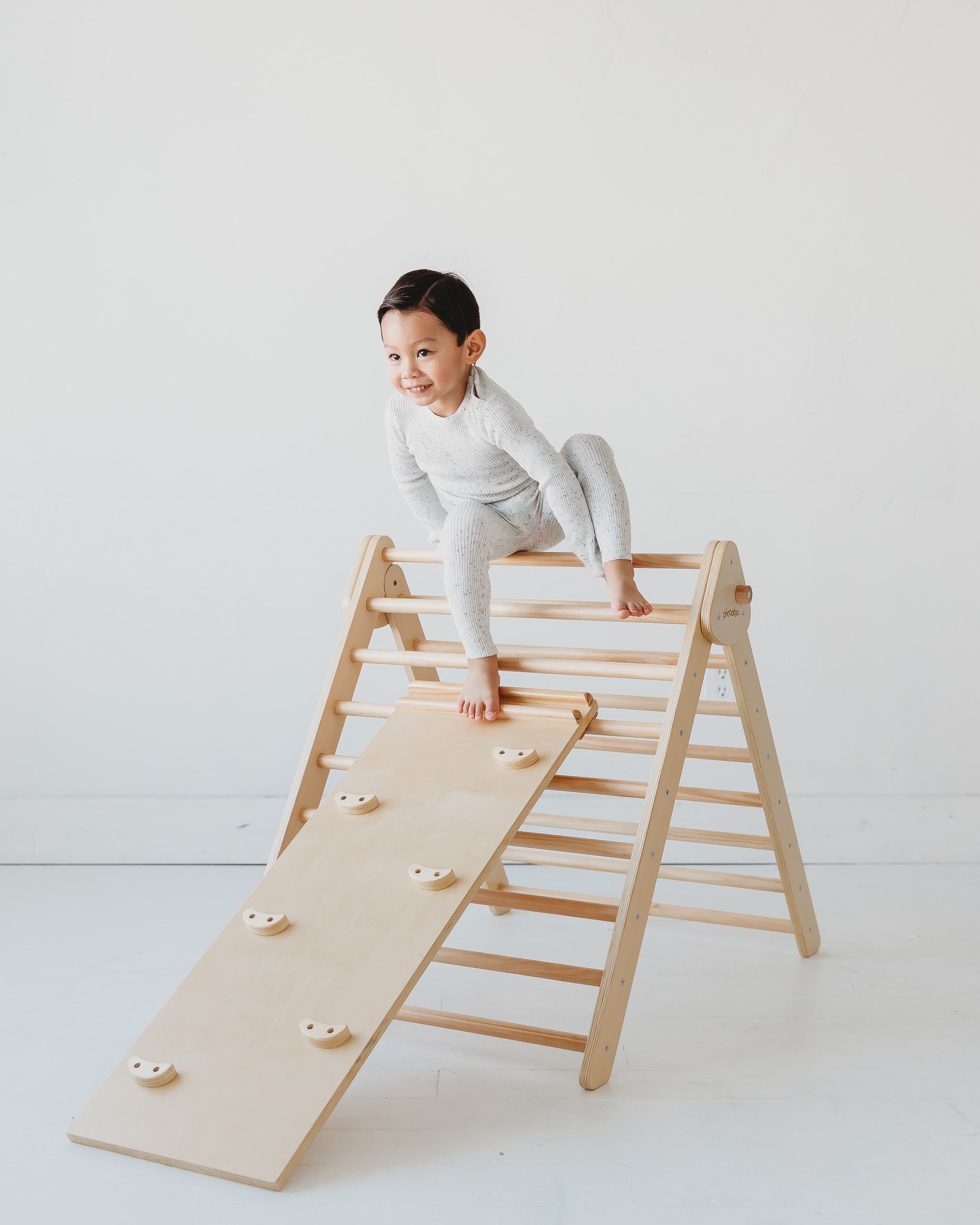 Piccalio Pikler Triangle in natural wood with a young boy climbing the triangle with a rock climbing ramp attachment.