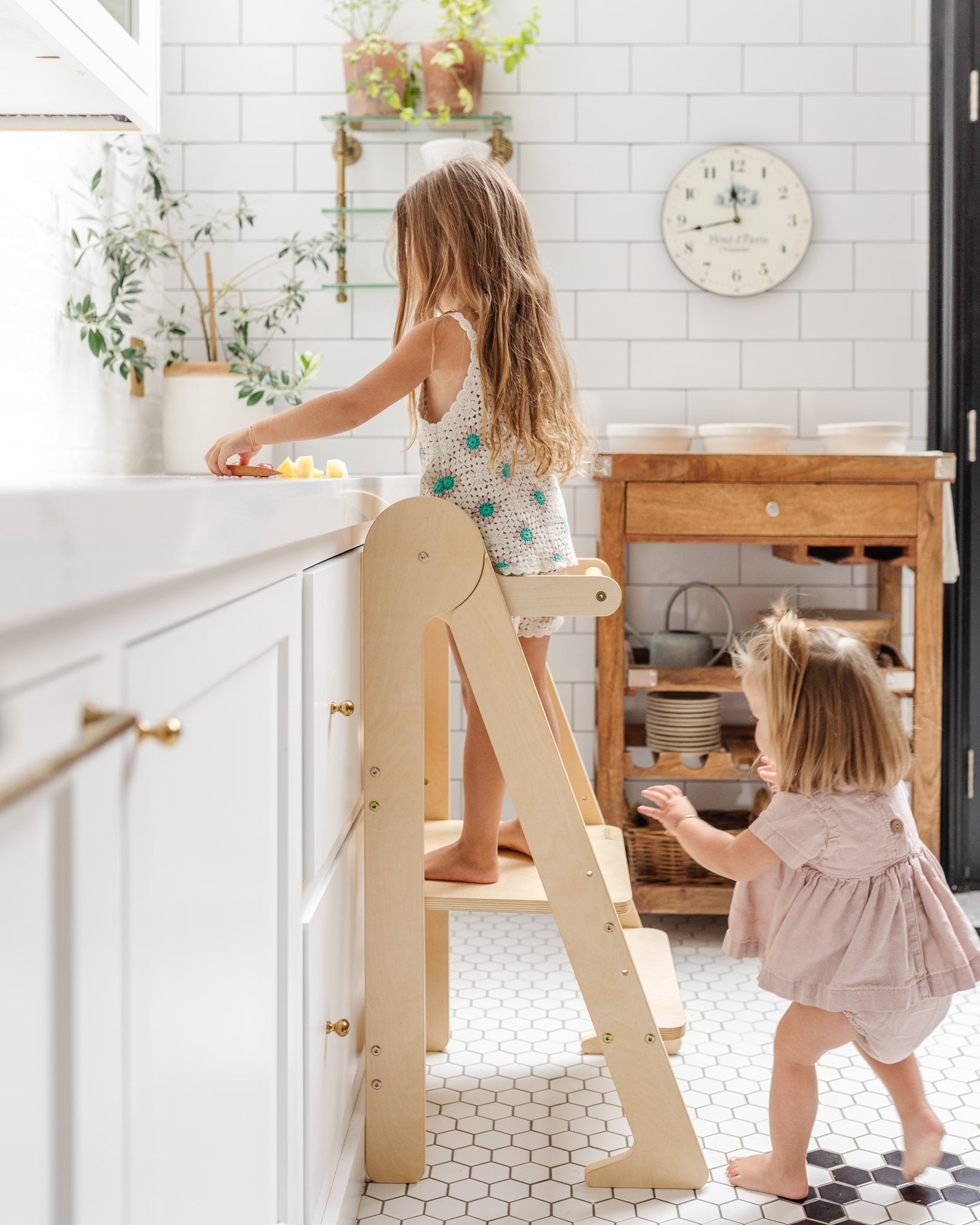 Two toddlers using the Piccalio wooden kitchen foldable toddler tower on a kitchen counter.