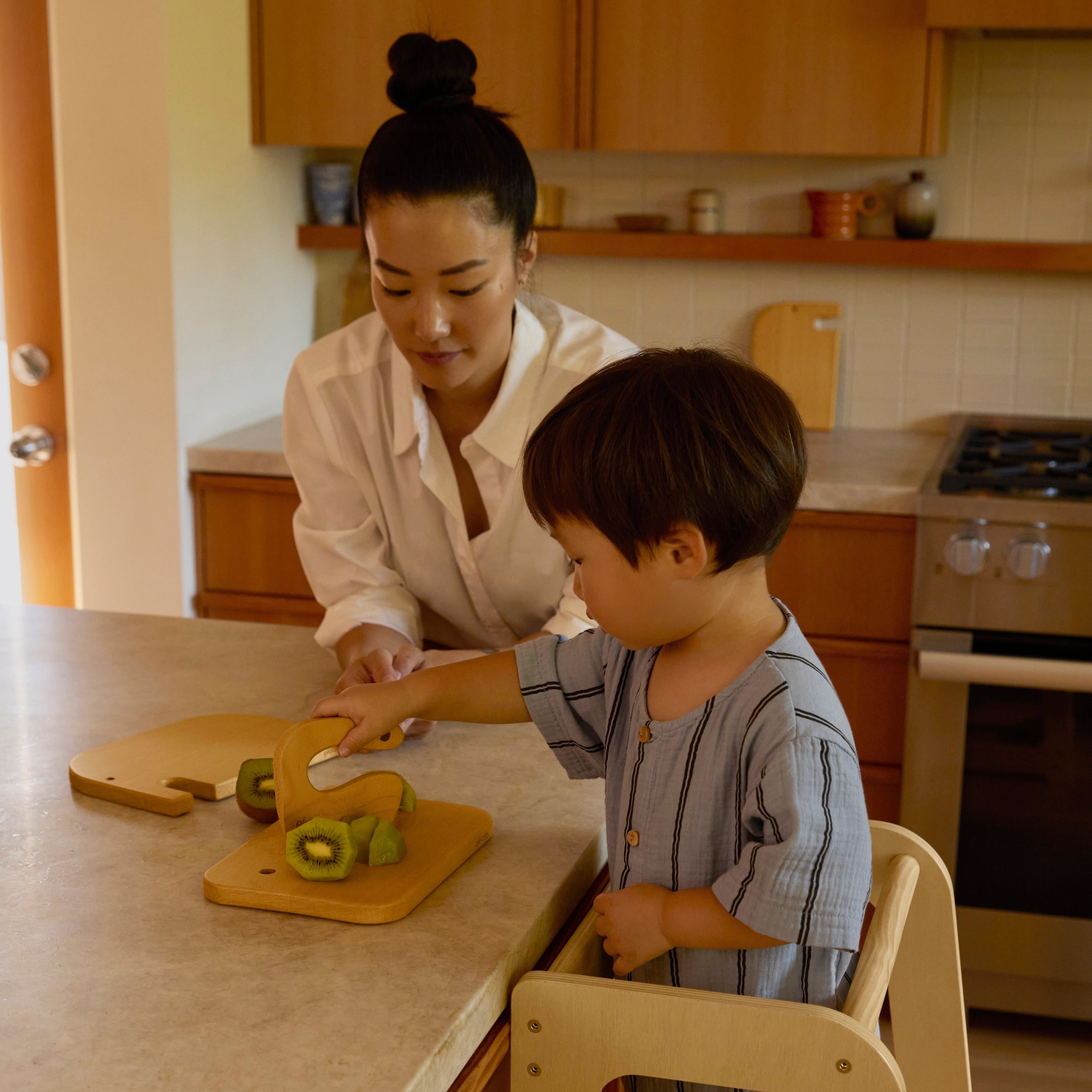 Child chopping fruit using the Piccalio Toddler Tower and cutting board made of natural wood