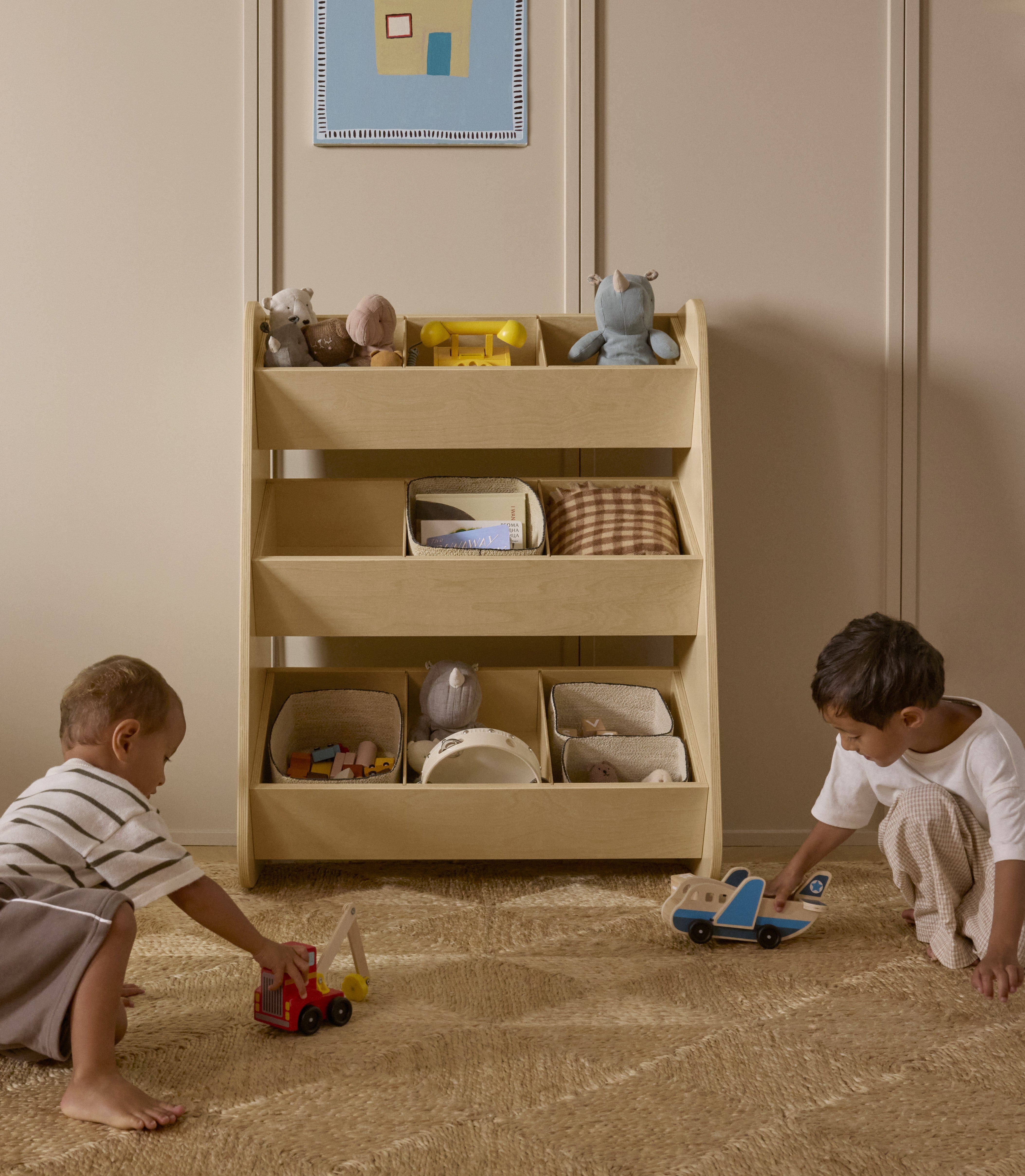 Toddlers playing with toys in front of an attractive toy organizer made of natural wood in a modern playroom