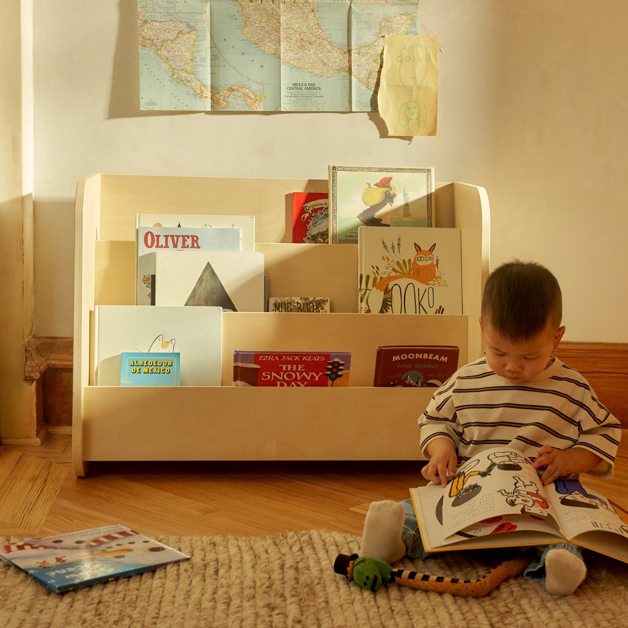 Boy reads a book in front of the Piccalio Montessori Bookshelf made of natural wood