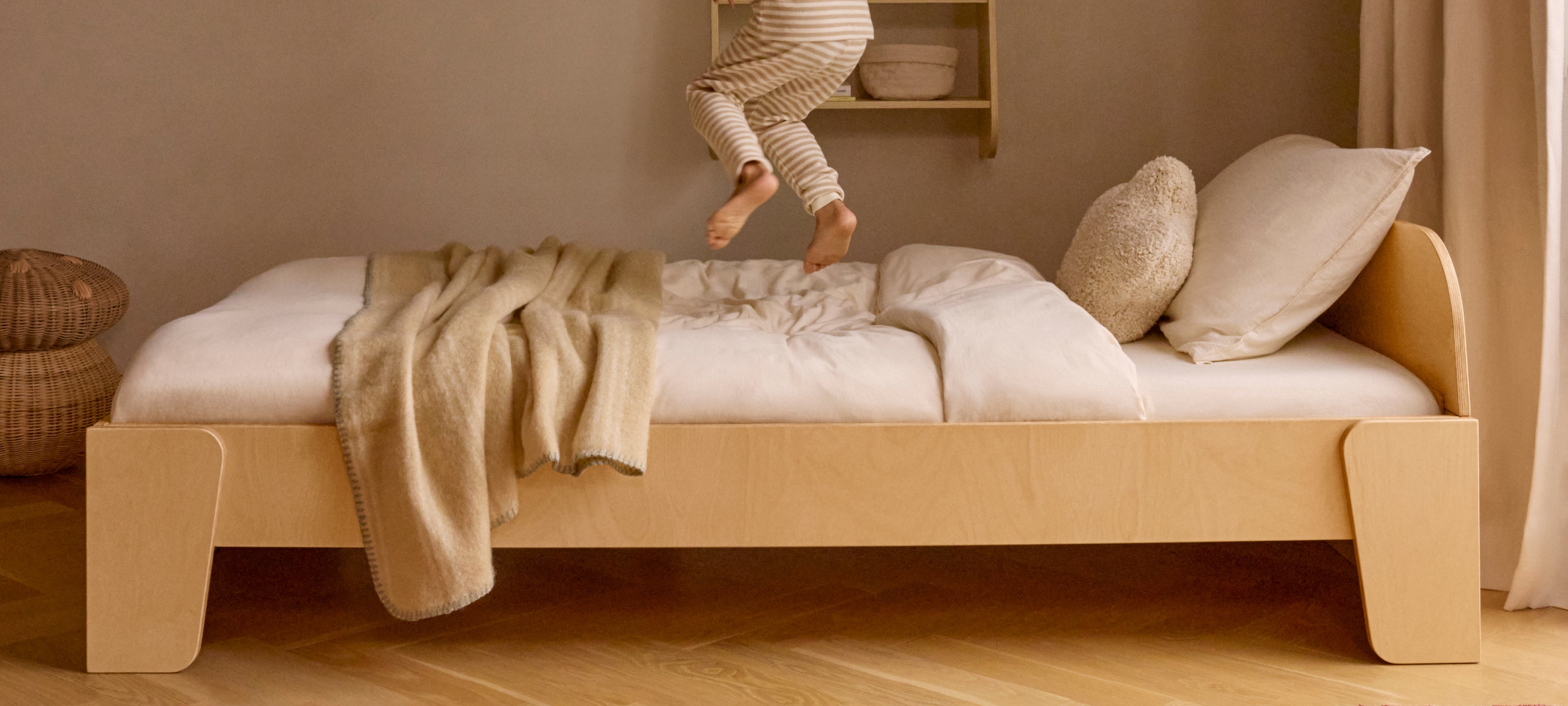 Montessori toddler bed with white bedding and a beige blanket on a wooden floor.