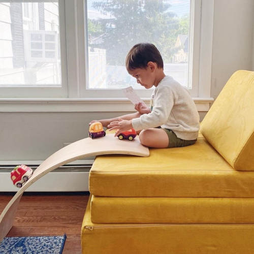 Child playing with a birch wood balance board for kids by turning it into a racetrack for toy cars