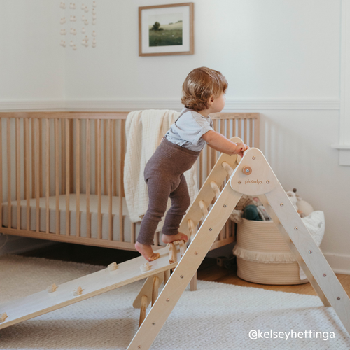 Toddler climbing the Piccalio Pikler triangle set with a rock wall and slide made of natural wood.