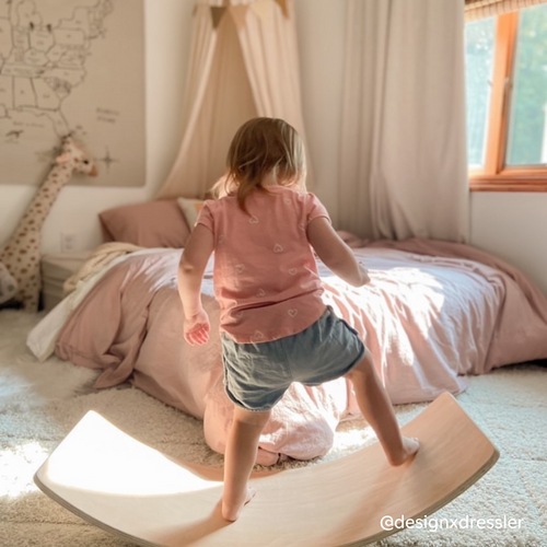 Girl balancing on a wooden balance board in her bedroom and enjoying independent active play