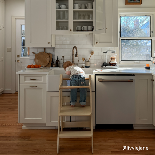 Toddler using kitchen helper tower made of natural birch wood at the kitchen sink