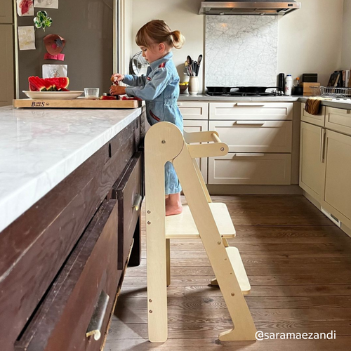 Child using Piccalio foldable learning tower in kitchen cutting watermelon