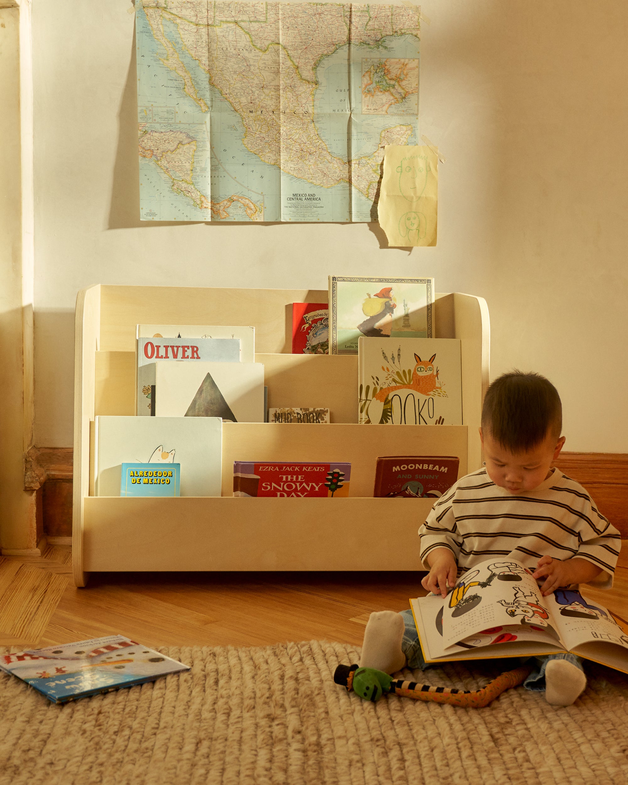 Child reading a book in front of Piccalio Montessori bookshelf with books and toys.