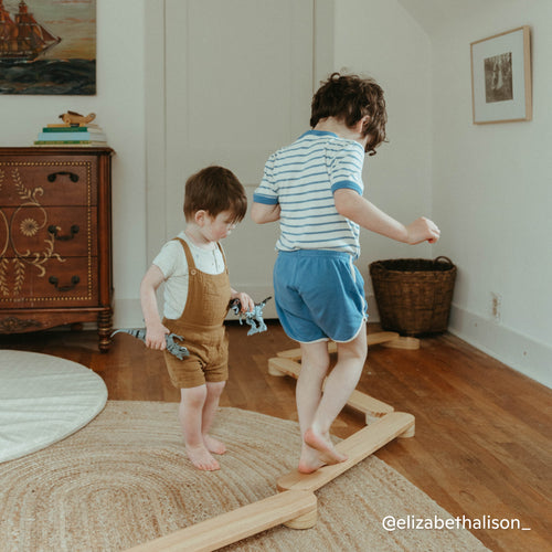 Two children balancing on Montessori balance beam made of natural wood in a children's bedroom
