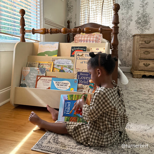 Child reading in front of the Piccalio Montessori bookshelf, a front-facing bookshelf made of birch wood