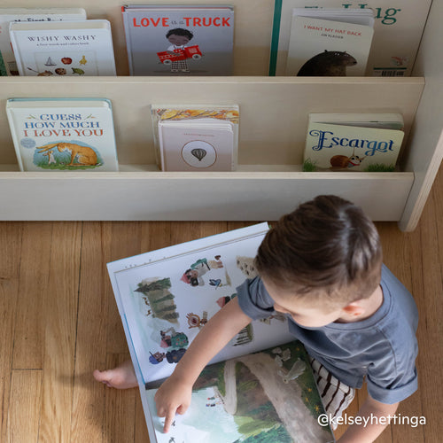 Child reading in front of front-facing Montessori bookshelf made of natural wood