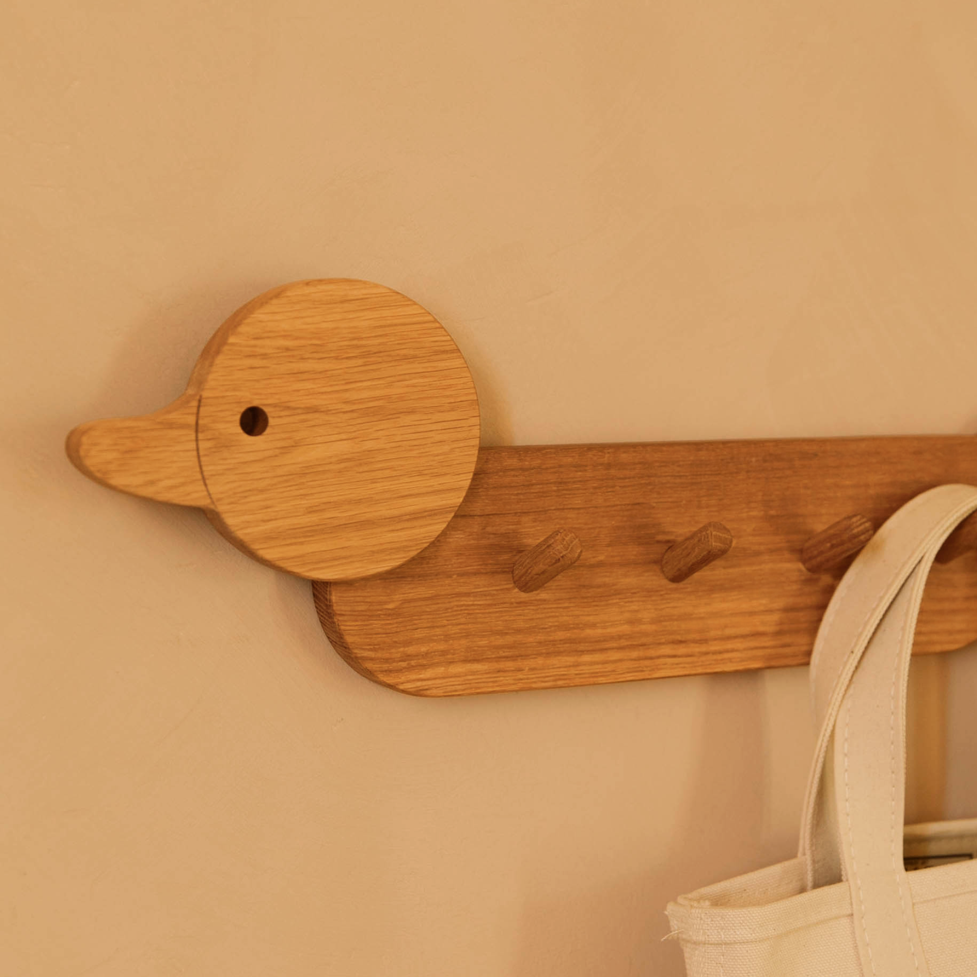 A canvas bag hangs on the duck shaped Piccalio Coat Rack for children made of oak wood 