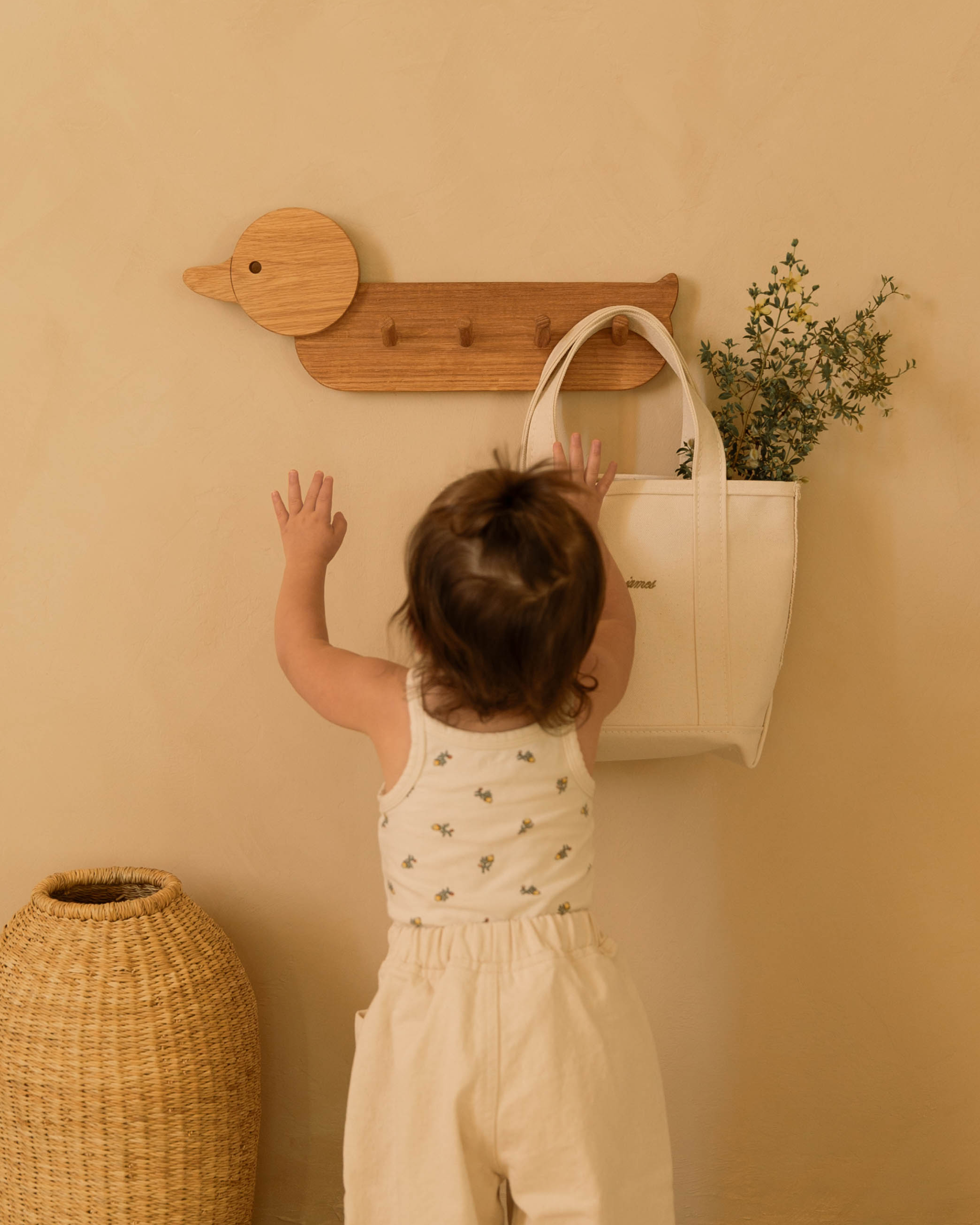 Child hanging a bag on the duck shaped Piccalio coat rack made of natural oak wood