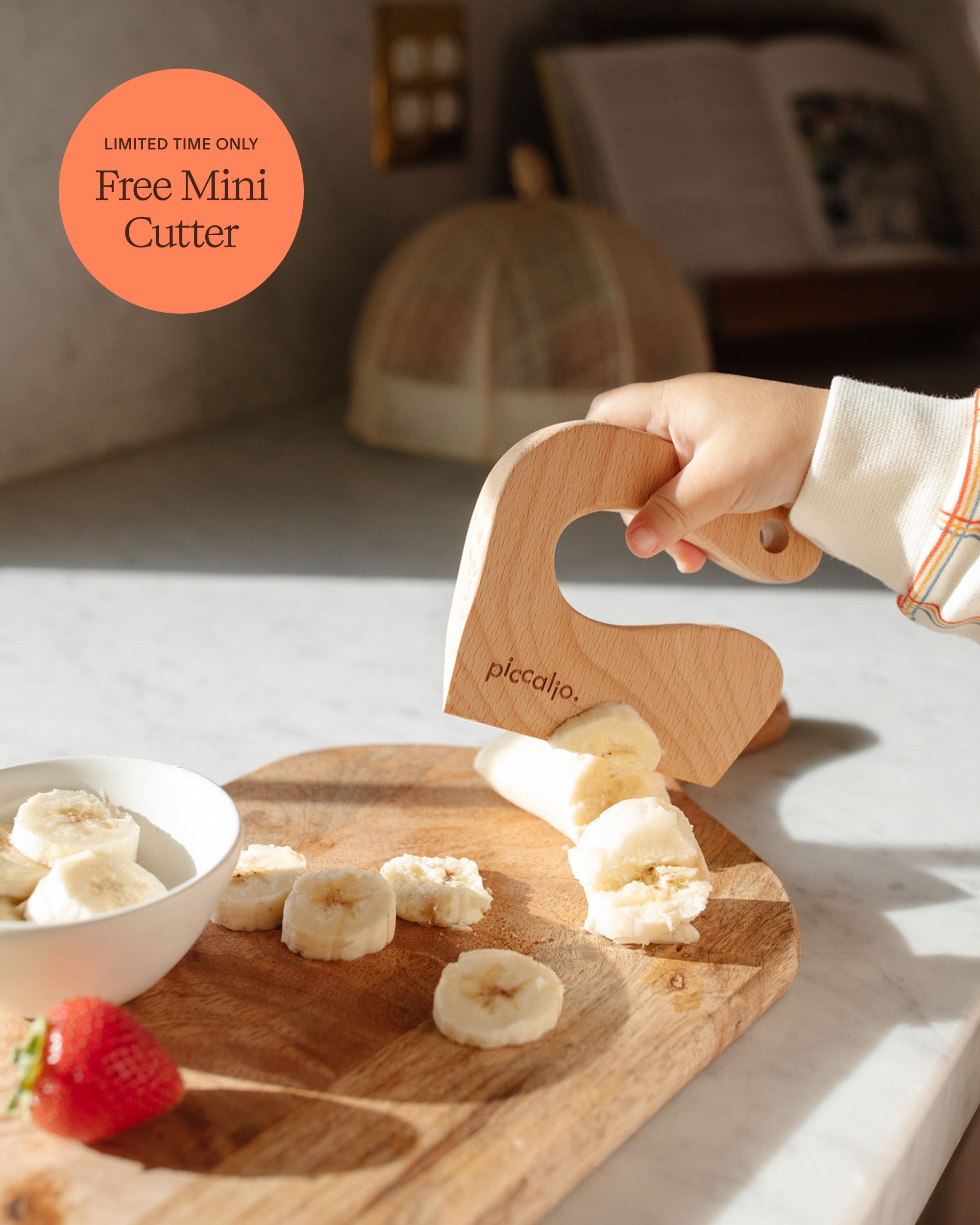 Close-up of a child safely slicing a banana with a Piccalio wooden mini cutter on a wooden board.