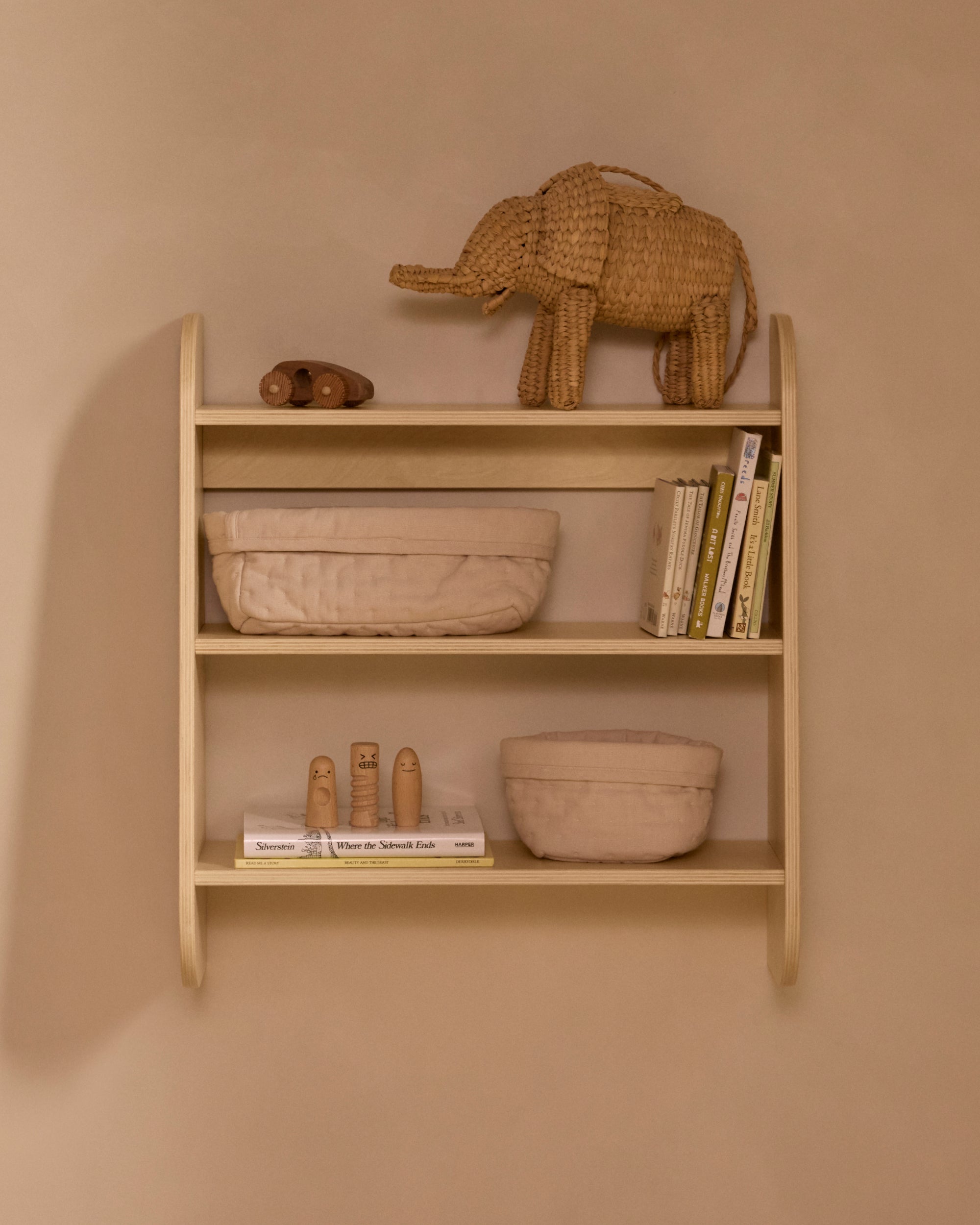 Piccalio birchwood wall shelf with three tiers holding books, toys, and baskets in a minimalist nursery.