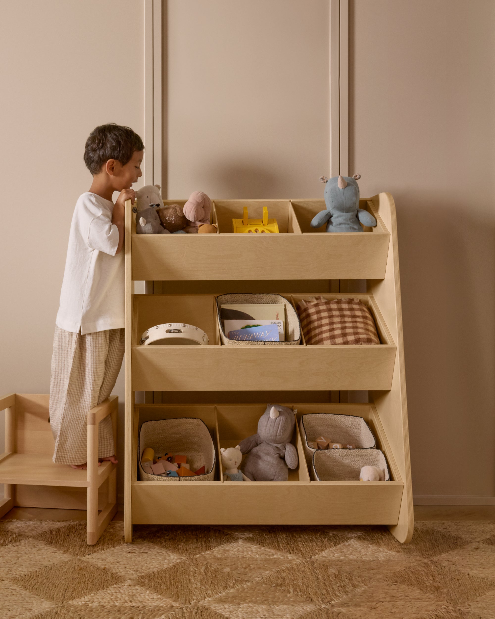 A child using a Piccalio birchwood tiered toy organizer with multiple cubbies for books, stuffed animals, and toys.