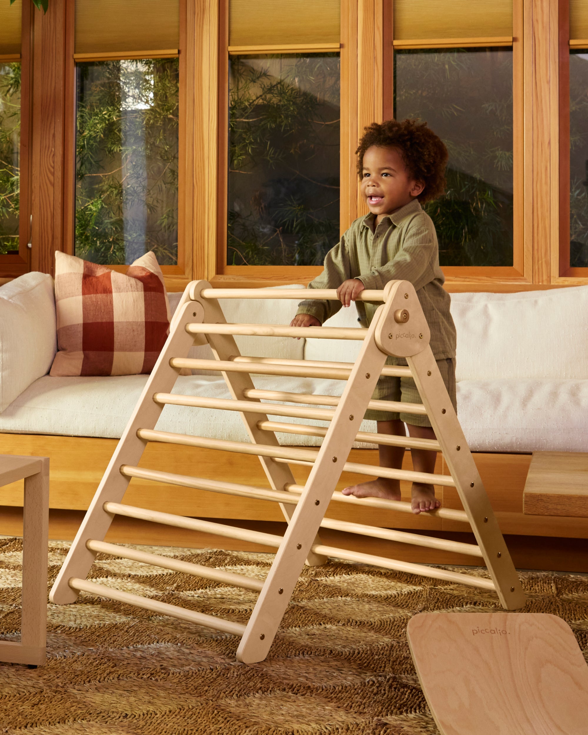 Piccalio Pikler Triangle in natural wood in a playroom with a toddler climbing to develop gross motor skills.