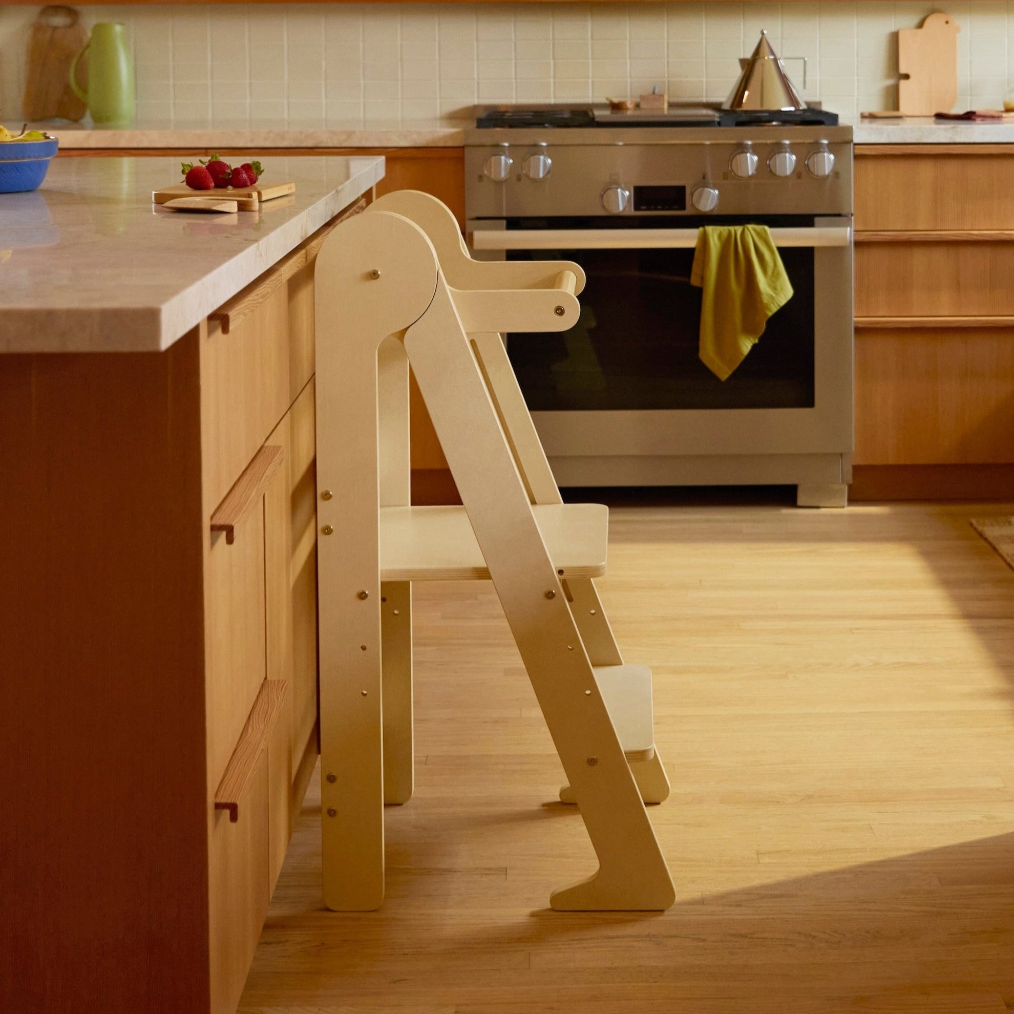 Piccalio foldable learning tower in a natural wood finish standing against a kitchen counter.