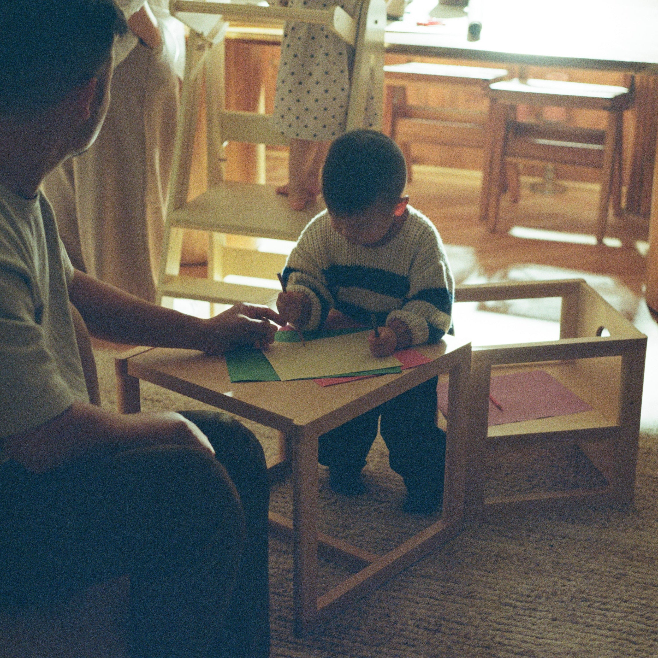 Piccalio kid table and chairs in natural wood used by a child drawing in a playroom.