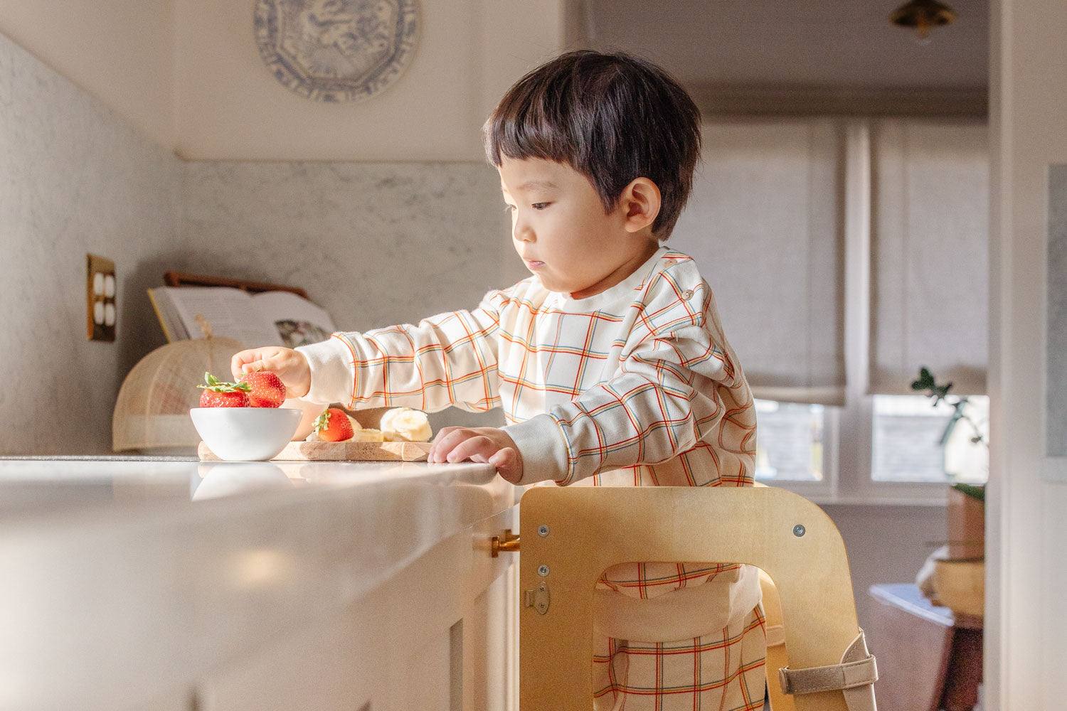 Piccalio convertible learning tower in natural birch wood used by a child at a kitchen counter.