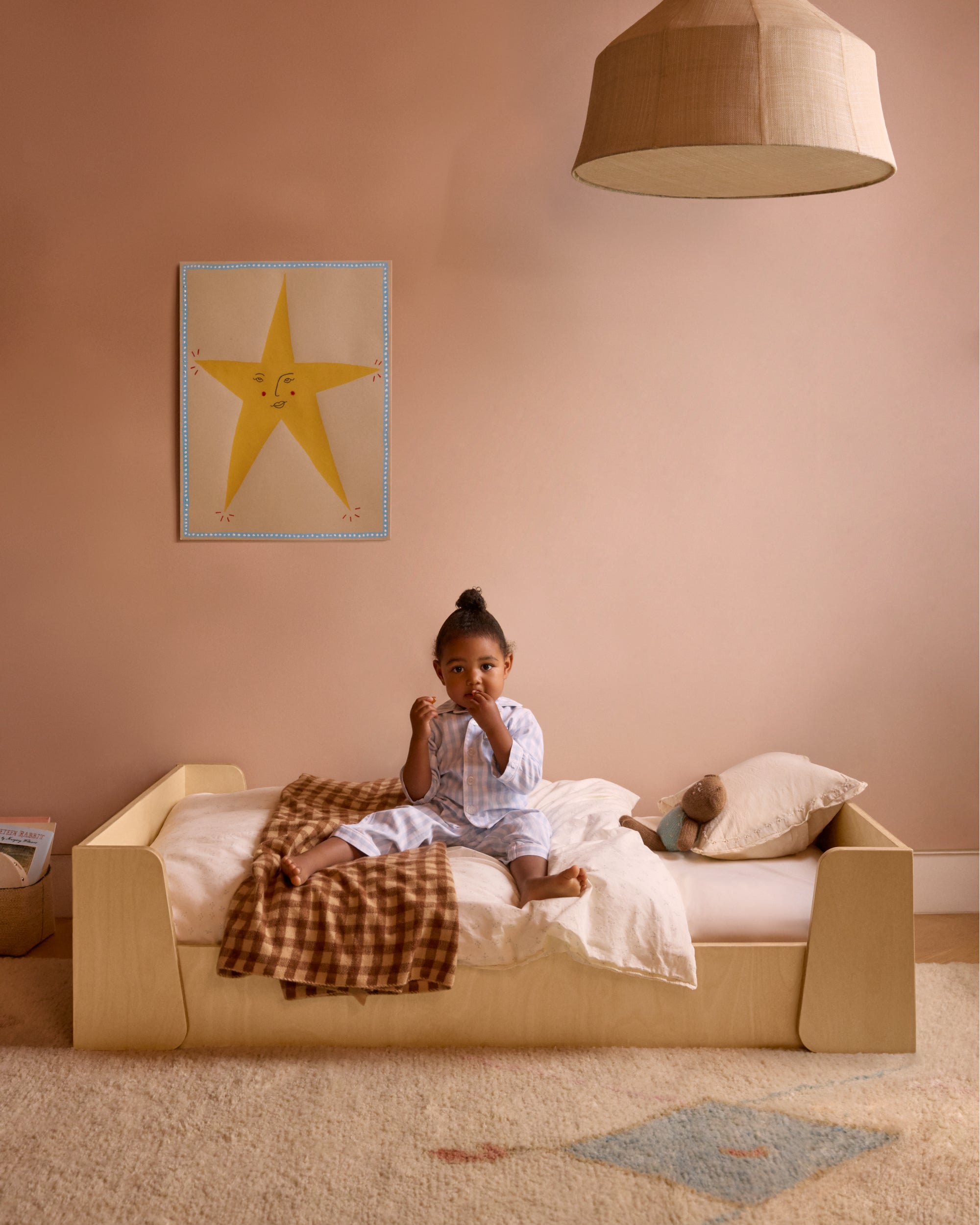 Piccalio toddler floor bed in natural wood with a toddler girl sitting in the bed.