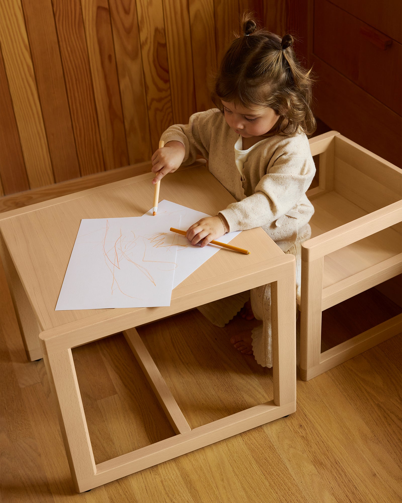 A minimalist Piccalio wooden play table and two stools in a natural beech finish, providing a child-sized activity station in a bright, modern nursery.
