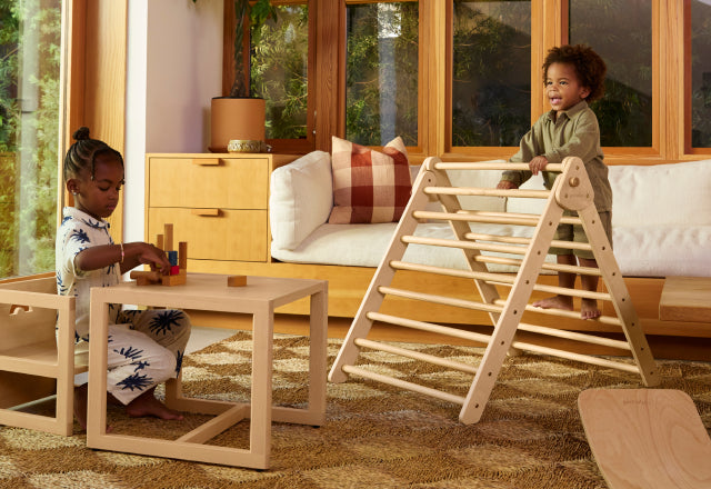 Children in living room playing on Pikler triangle and sitting at play table and chair