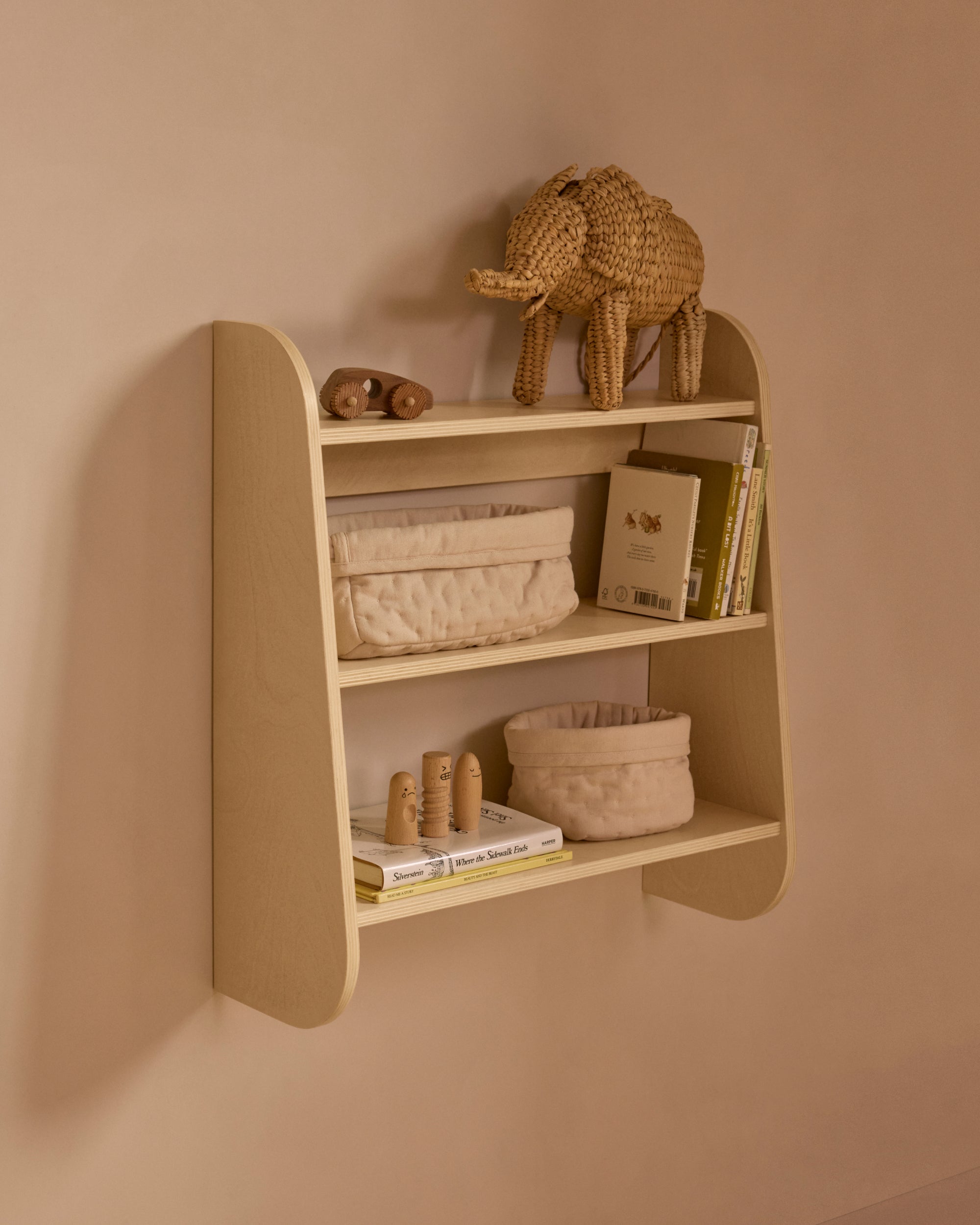 Angled view of a Piccalio three-tier wooden nursery shelf with books and minimalist decor.