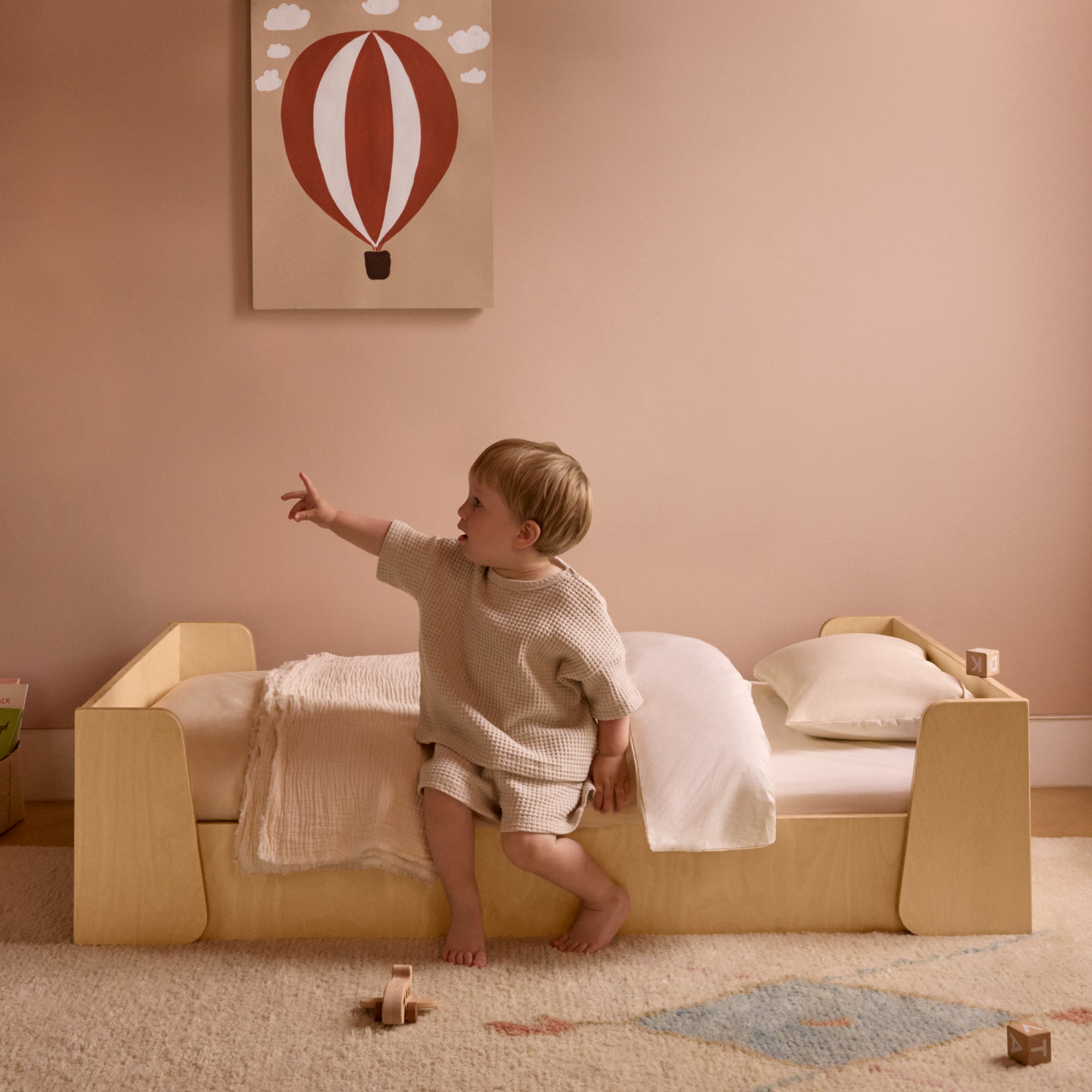 Toddler playing on a low-to-the-ground Montessori bed frame.