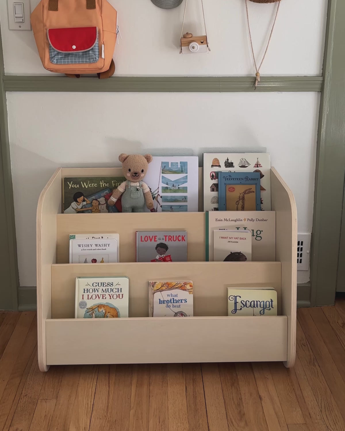 Piccalio montessori bookshelf storage against the bedroom wall with a toddler reading and putting books away.