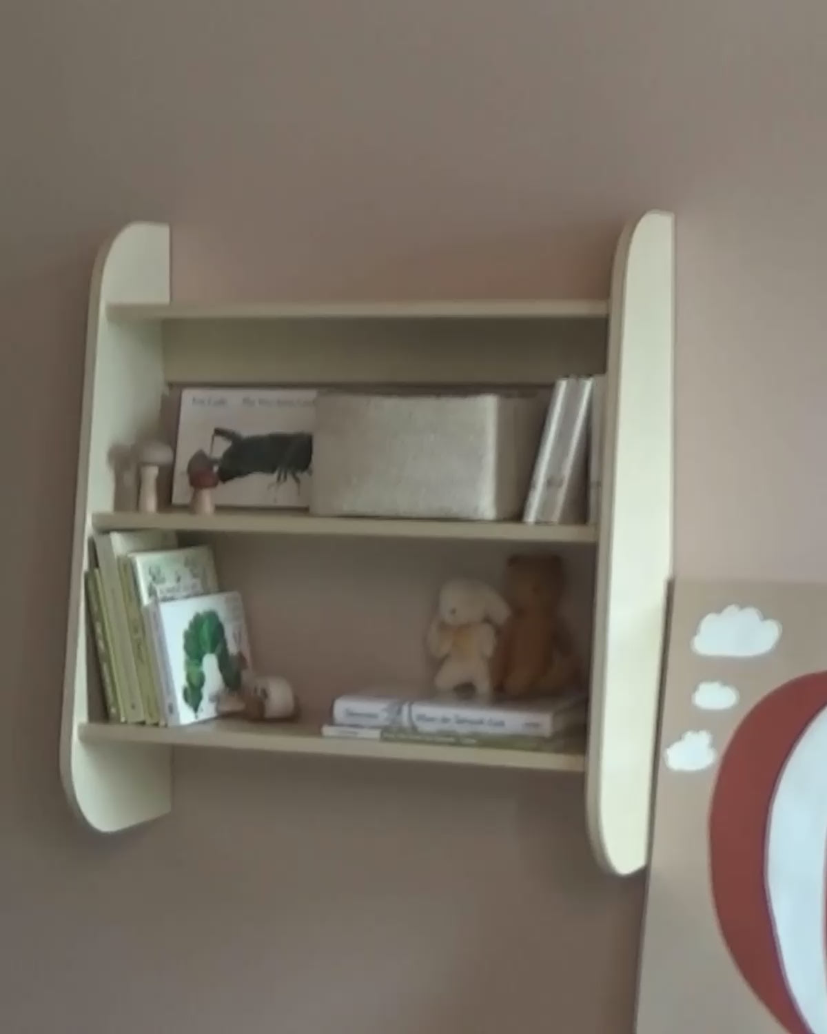 Child arranges wooden number blocks on a Piccalio three-tier birchwood Wall Shelf styled with picture books, a woven basket, and stuffed animals in a Montessori nursery.