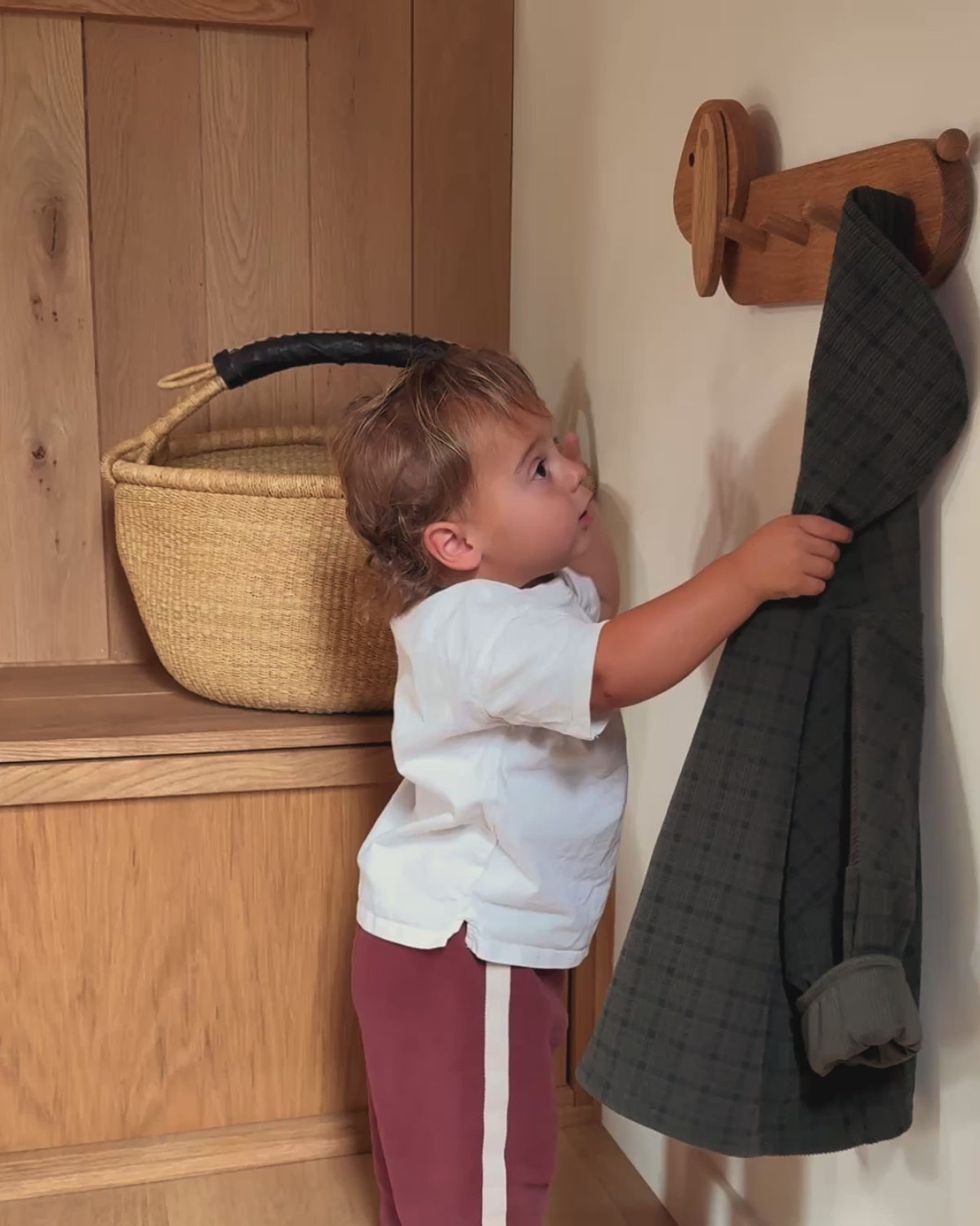 Child using Piccalio Coat Rack made of natural oak wood, practicing Montessori independence.