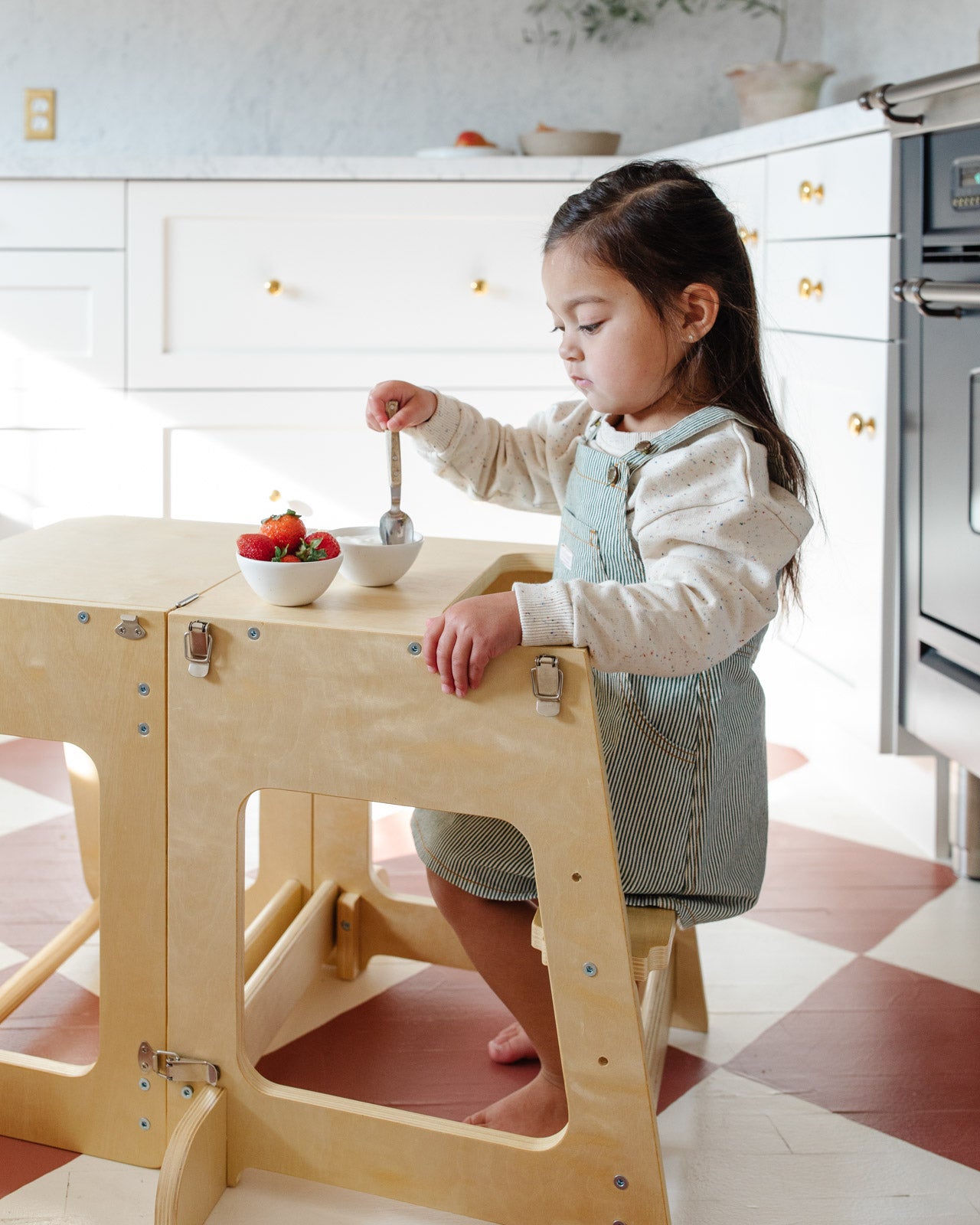 Piccalio kitchen helper tower used by a toddler sitting at the desk configuration eating strawberries.